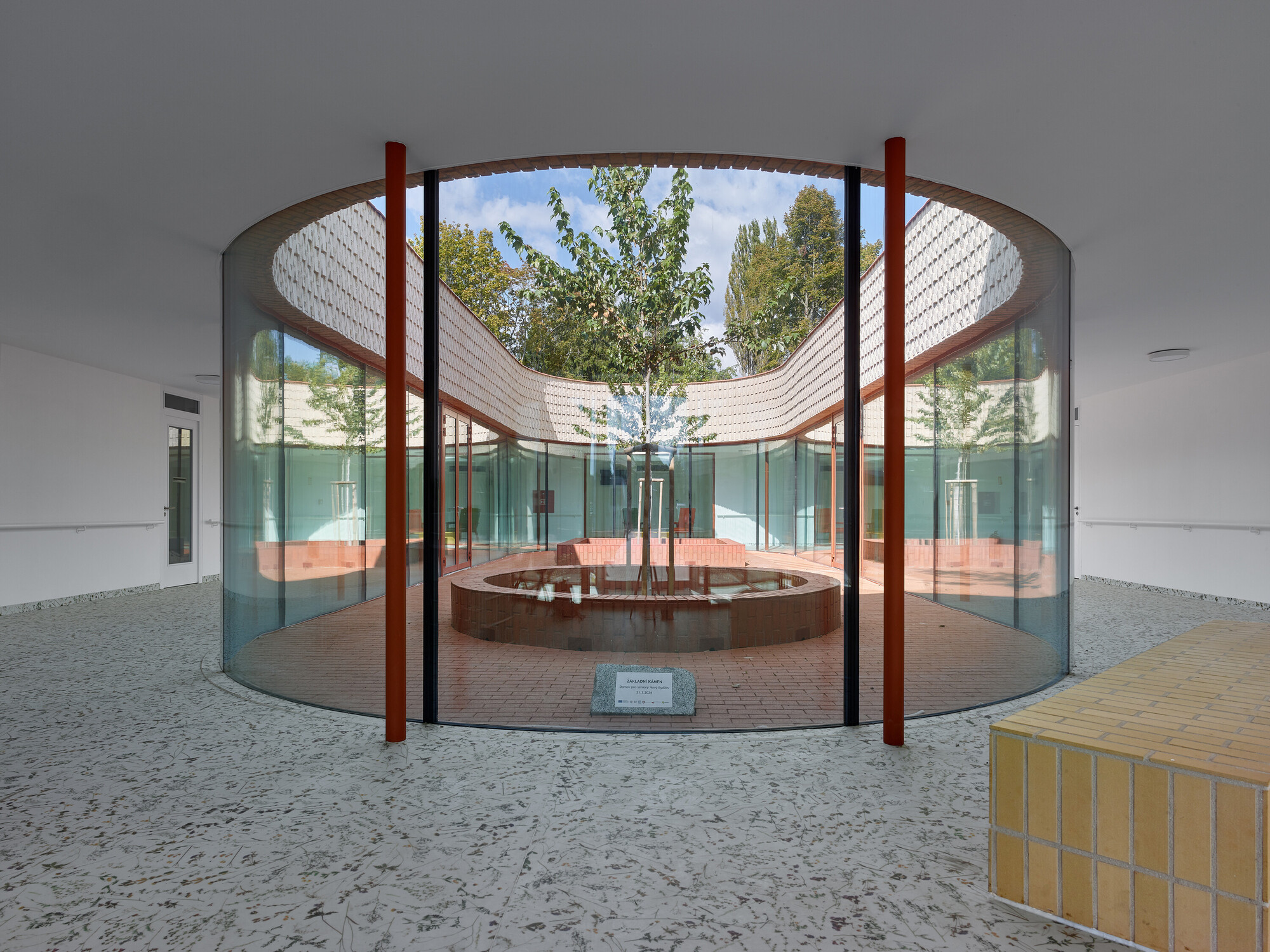 Circular courtyard with curved timber canopy over a central tree and terrazzo floor