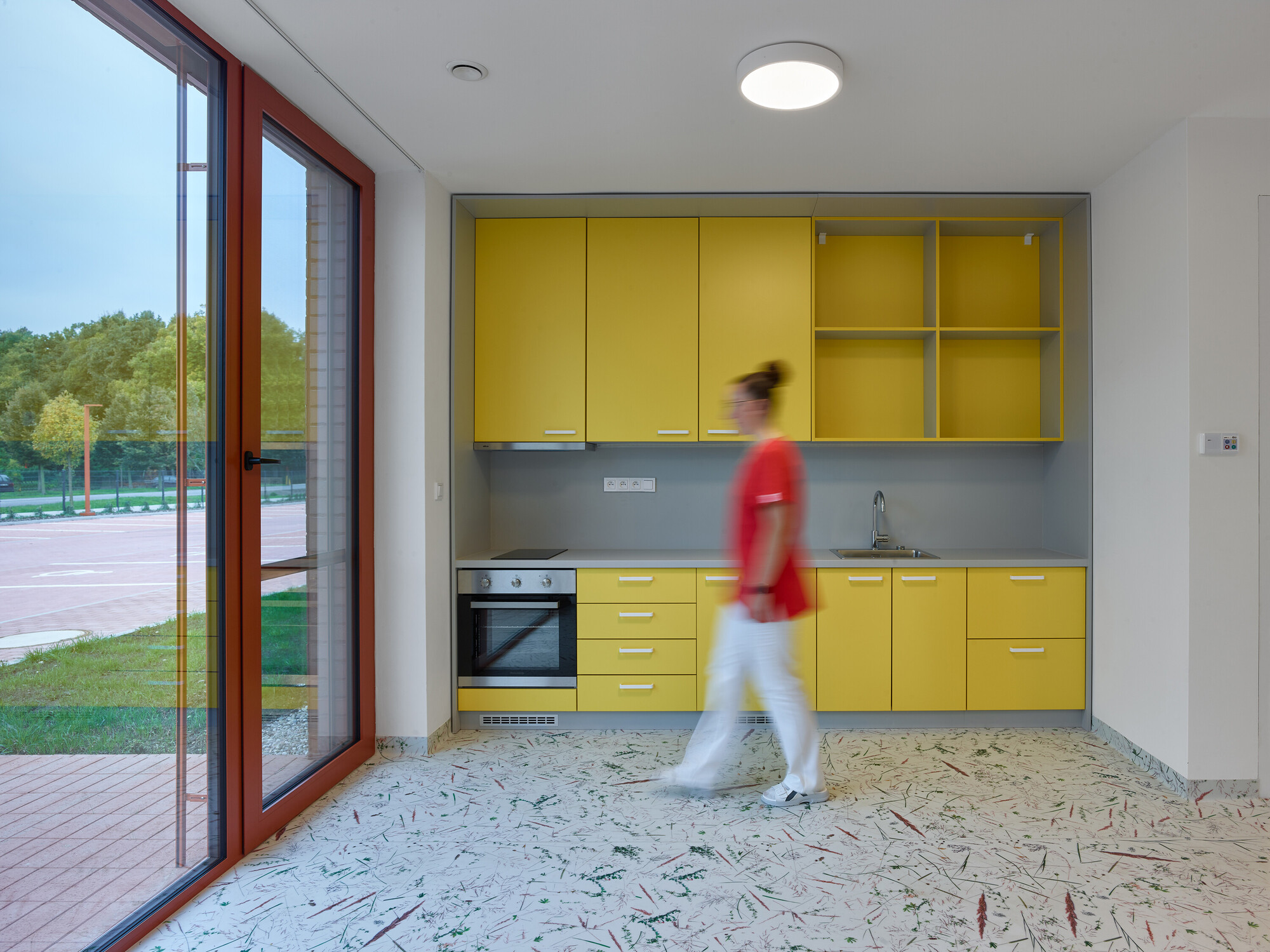 Yellow cabinetry with a person walking past toward the glazed door opening onto the sports court