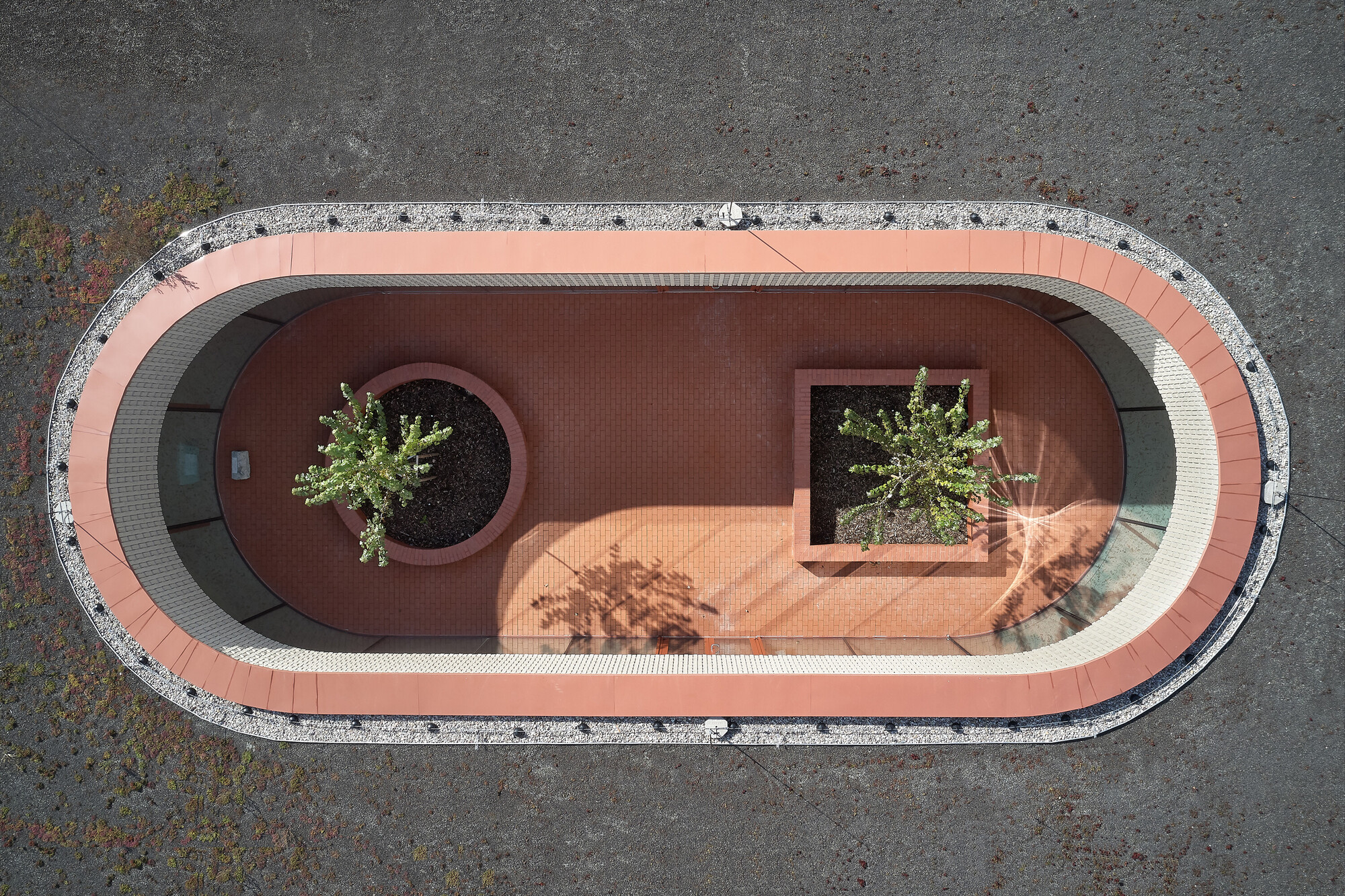 Aerial view of oval courtyard with red tile paving, circular and square planters, and gravel border