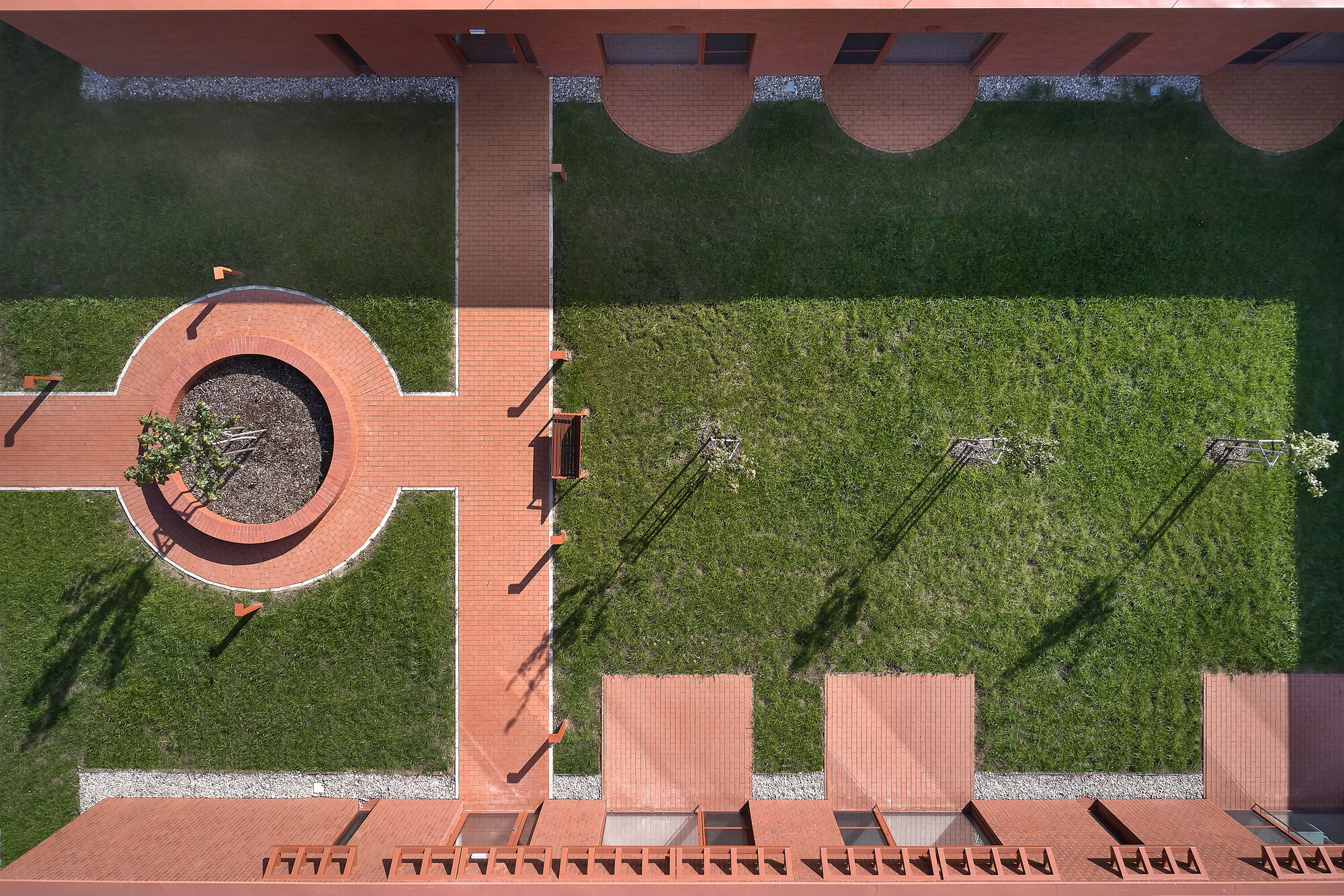 Overhead view of red tile terrace with circular planter, lawn areas, and person walking along the path