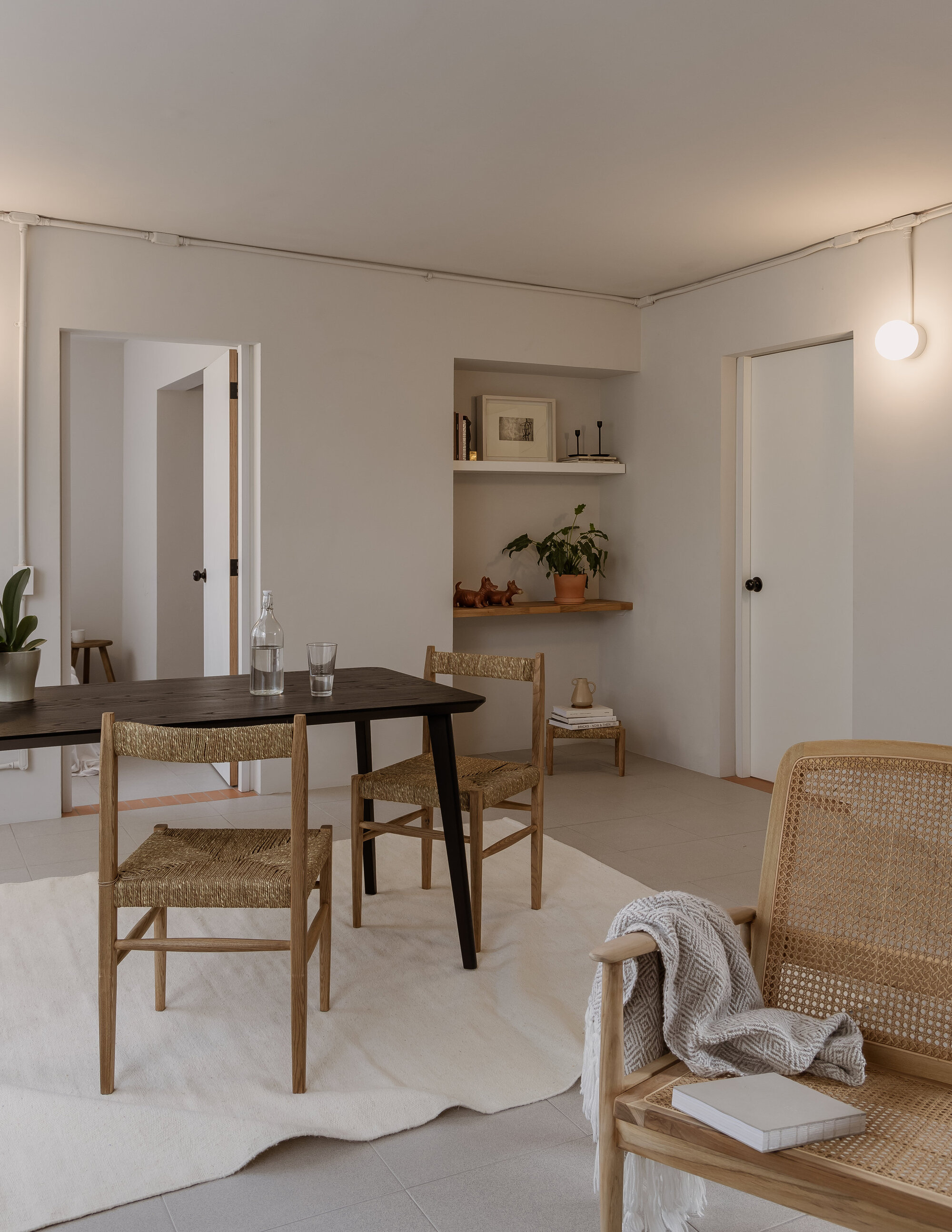Dining area with woven rush chairs around a dark timber table and built-in shelving with potted plant