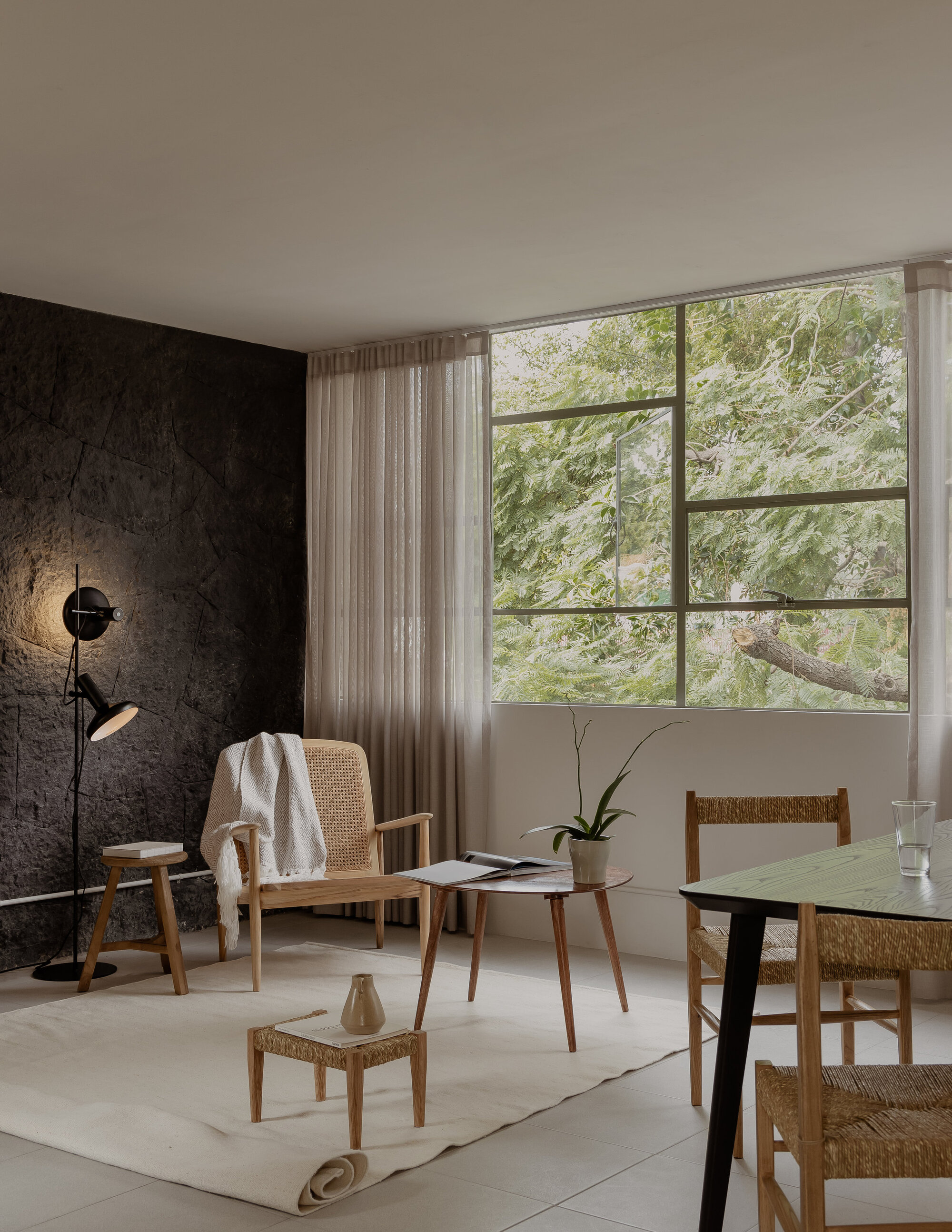 Living space with gridded steel window framing a tree canopy and textured dark feature wall
