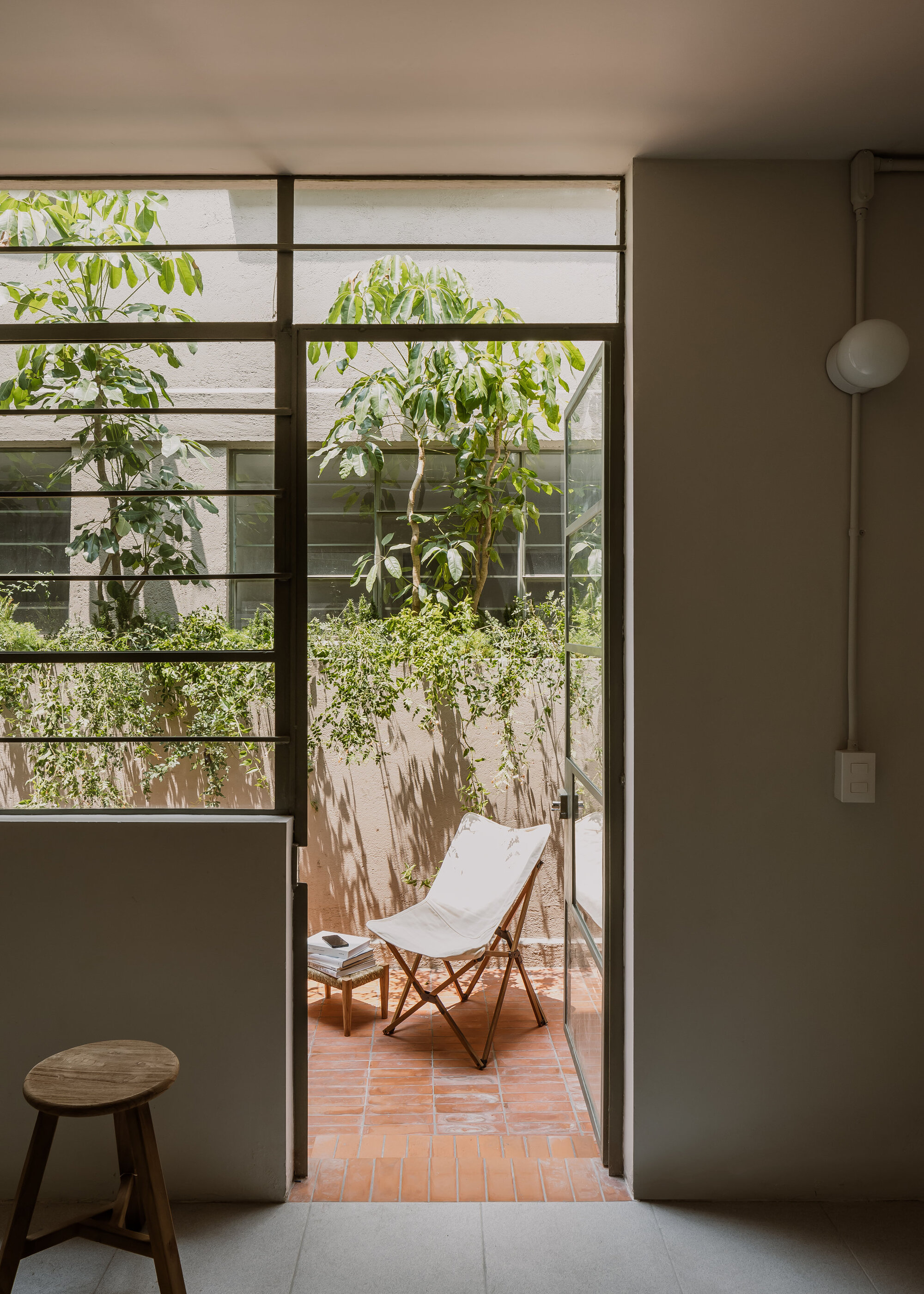 Glass door opening onto a terrace with a folding chair beneath green foliage