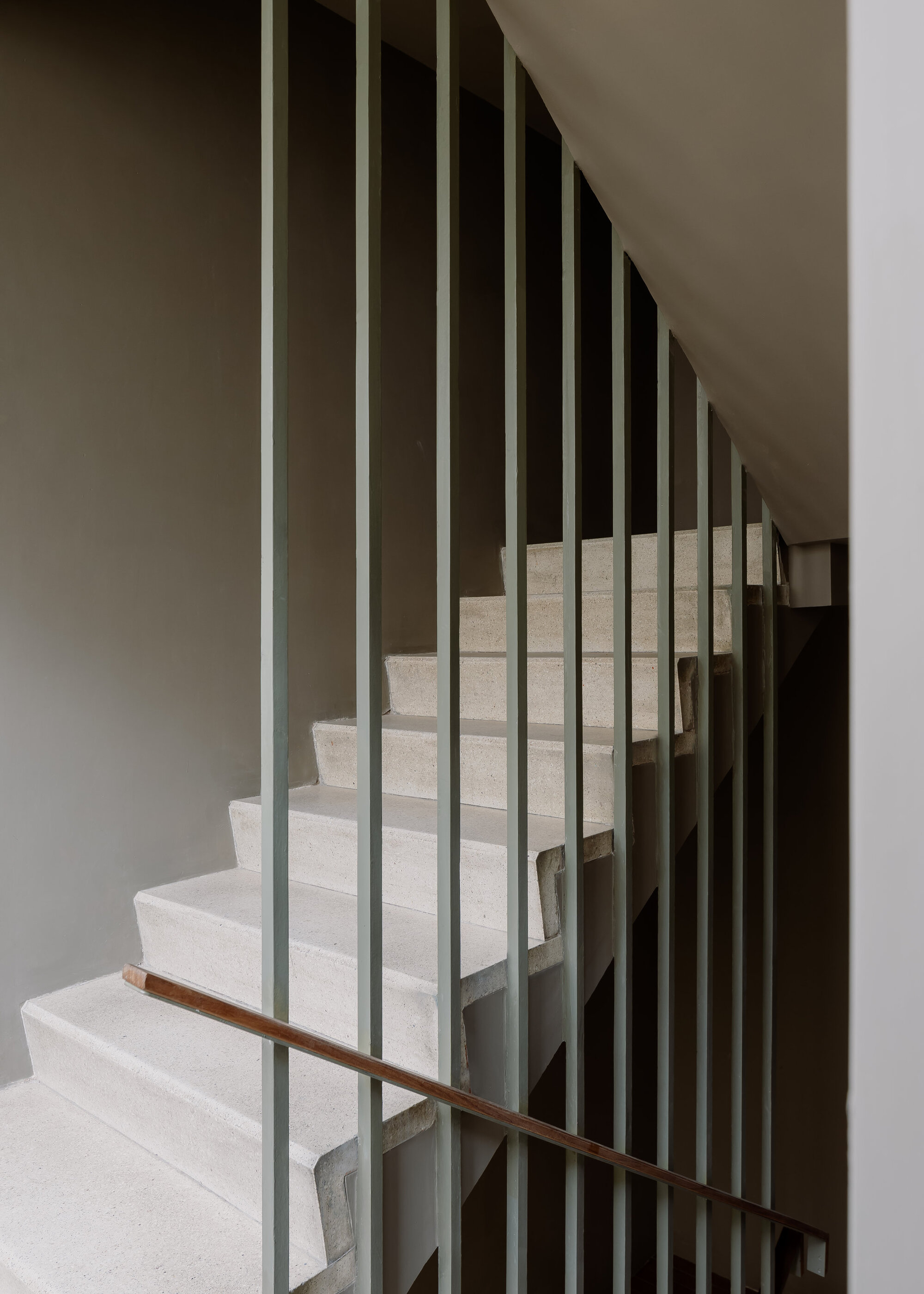 Staircase with vertical metal balusters and a timber handrail ascending between white walls