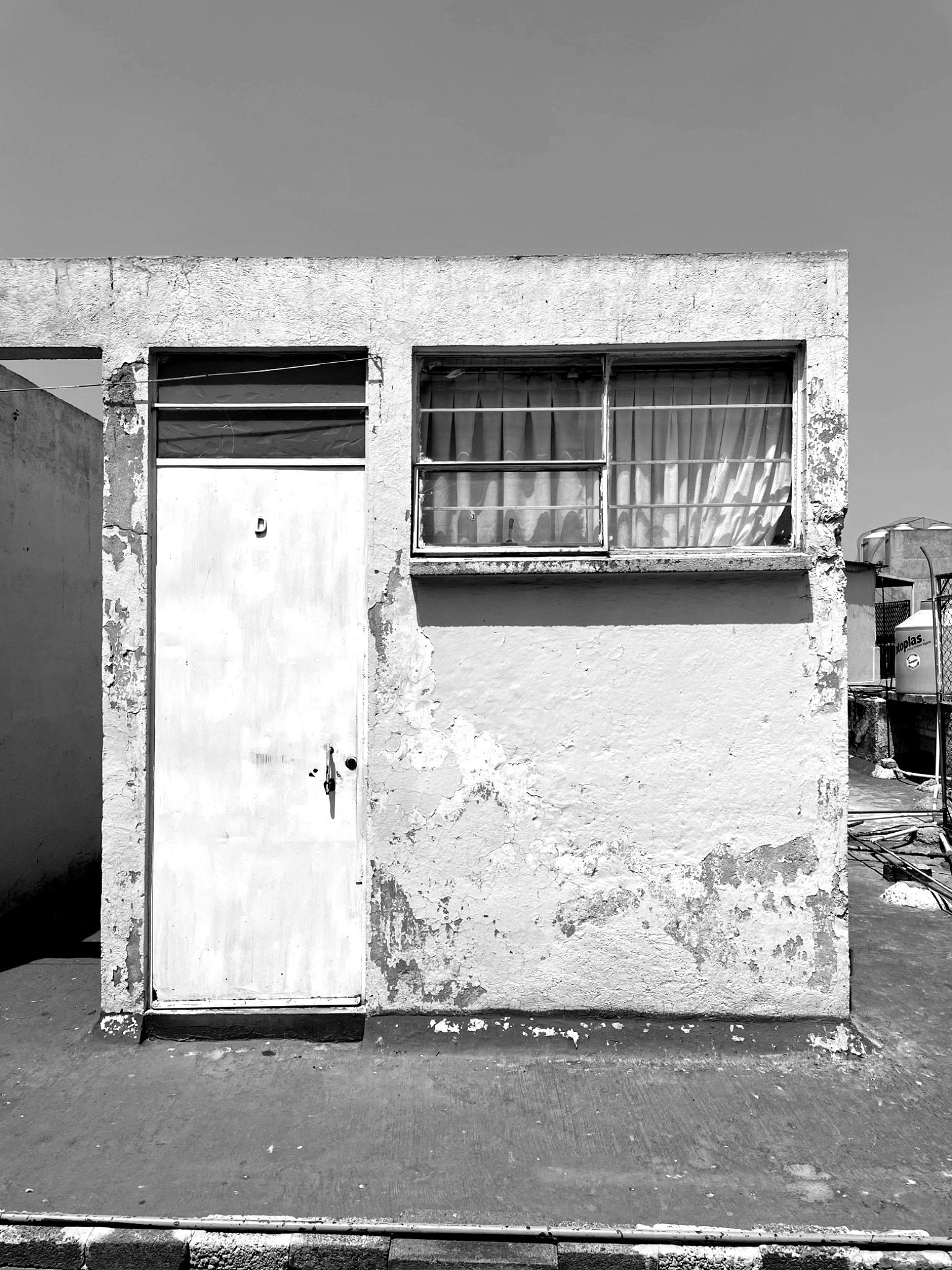 Weathered concrete facade with metal door and horizontal window under direct sunlight