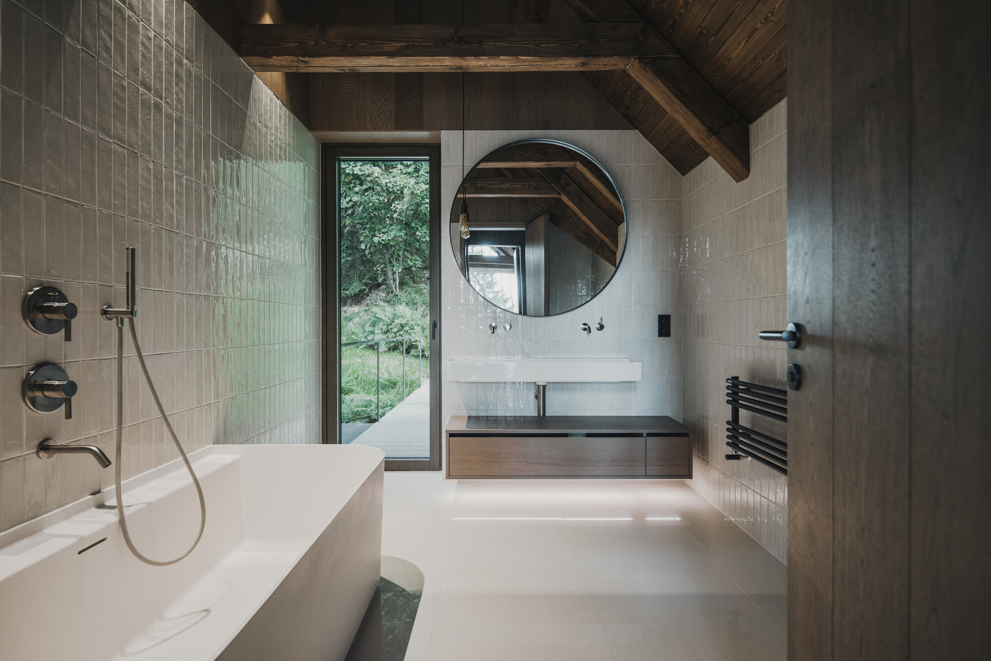 Bathroom with white tile walls, timber ceiling beams, and a door opening to greenery