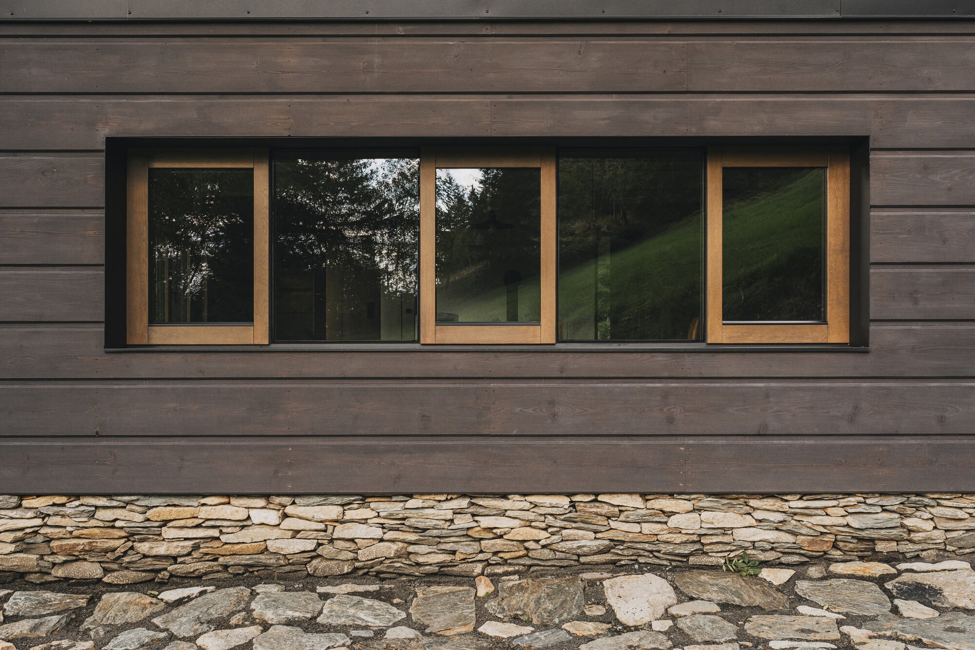 Horizontal timber cladding with ribbon window above fieldstone paving at grade