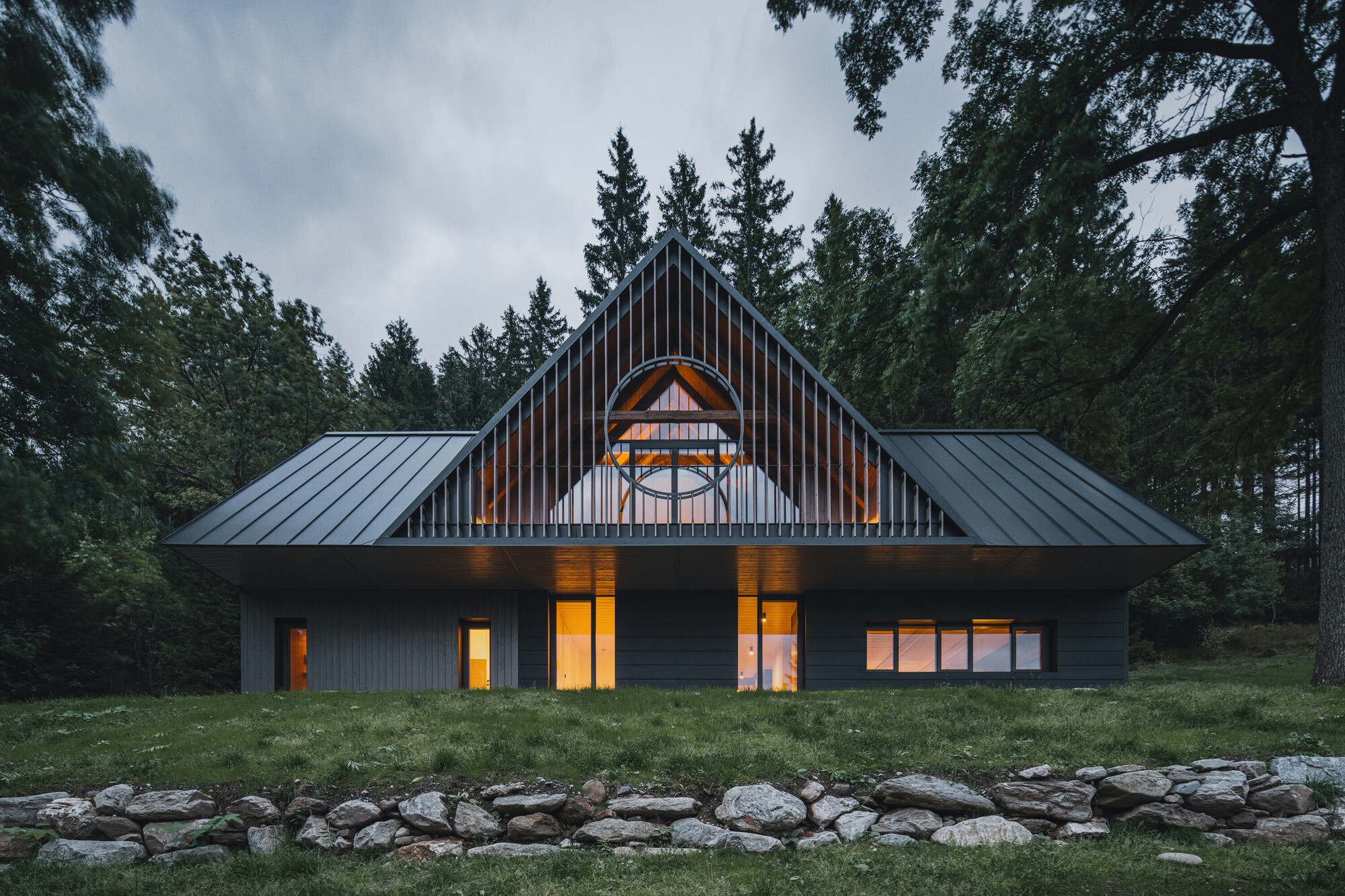 Front elevation showing symmetrical gable with arched window and stone retaining wall in evening light