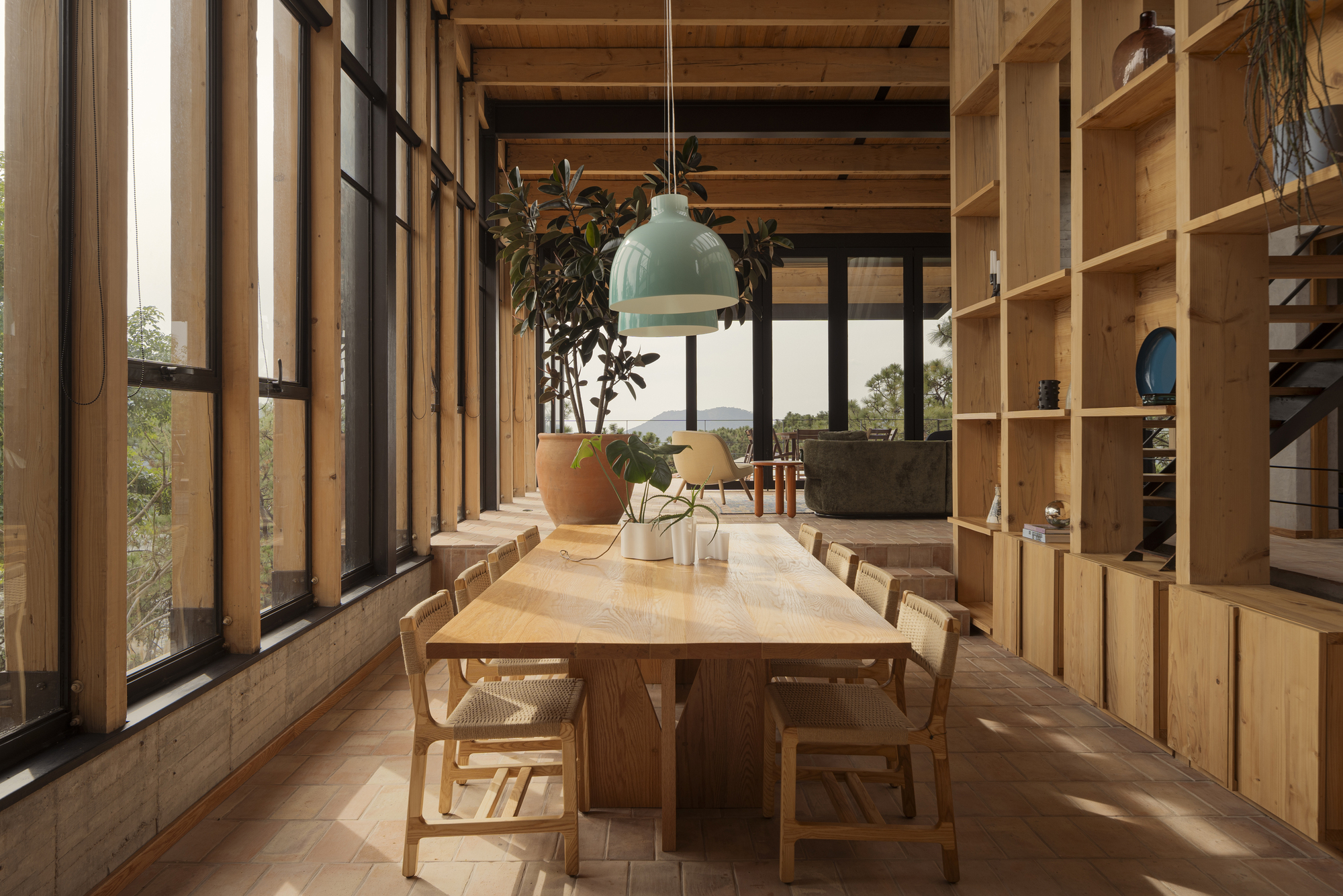 Dining area with exposed timber ceiling beams and floor-to-ceiling plywood shelving under soft afternoon light