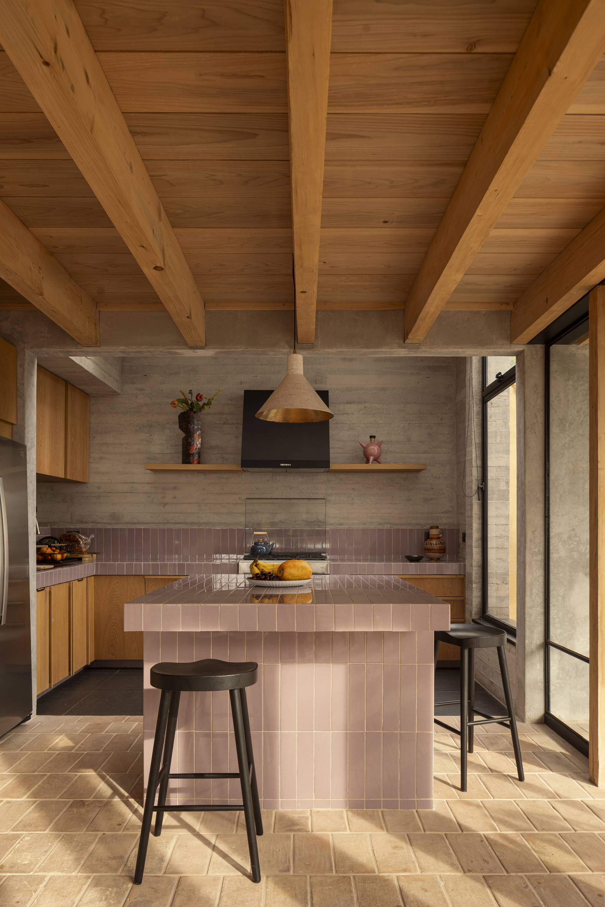 Kitchen with pink tiled island and board-formed concrete backsplash under an exposed timber joist ceiling