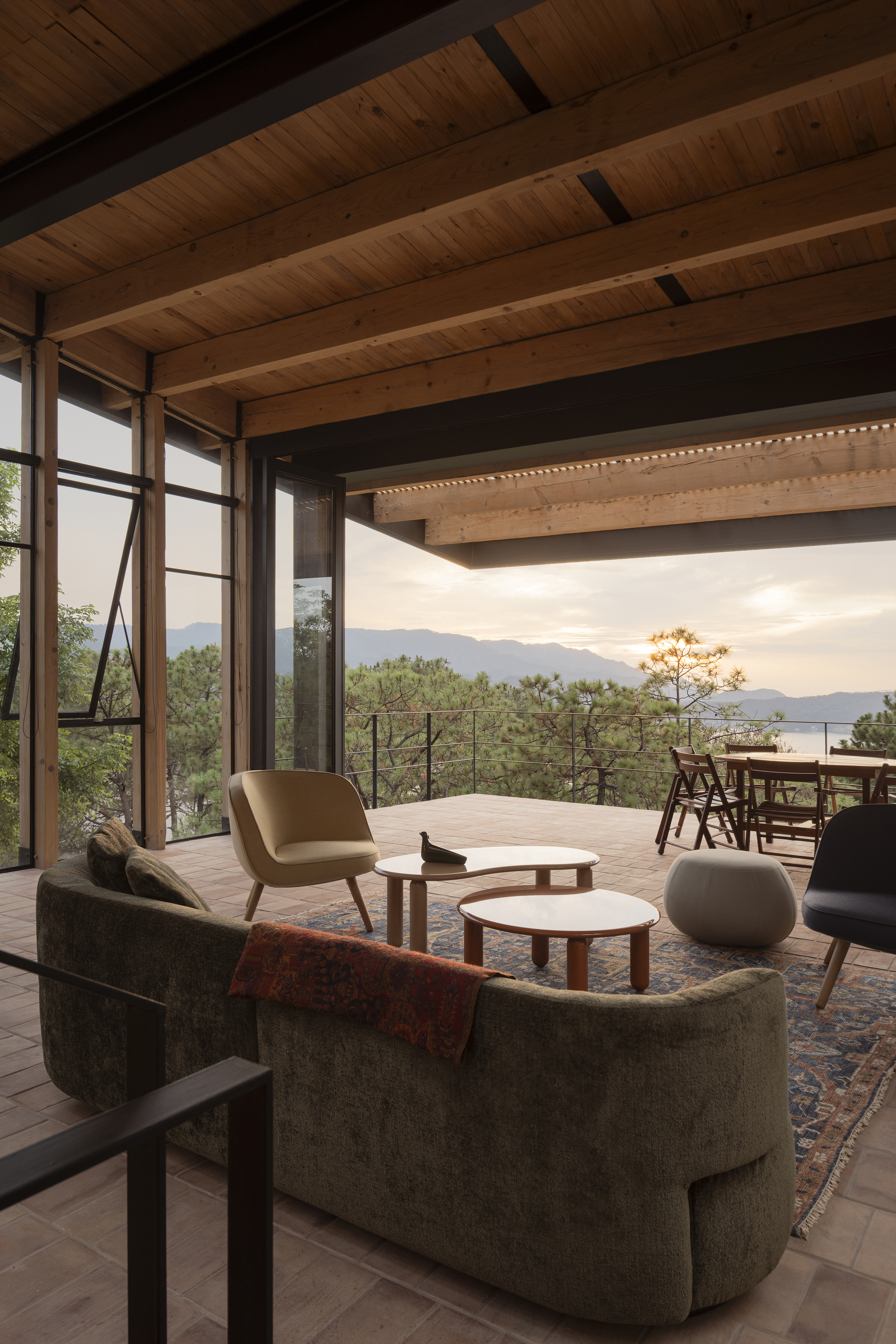 Living room with curved sofa looking through steel-framed windows toward distant mountains at dusk