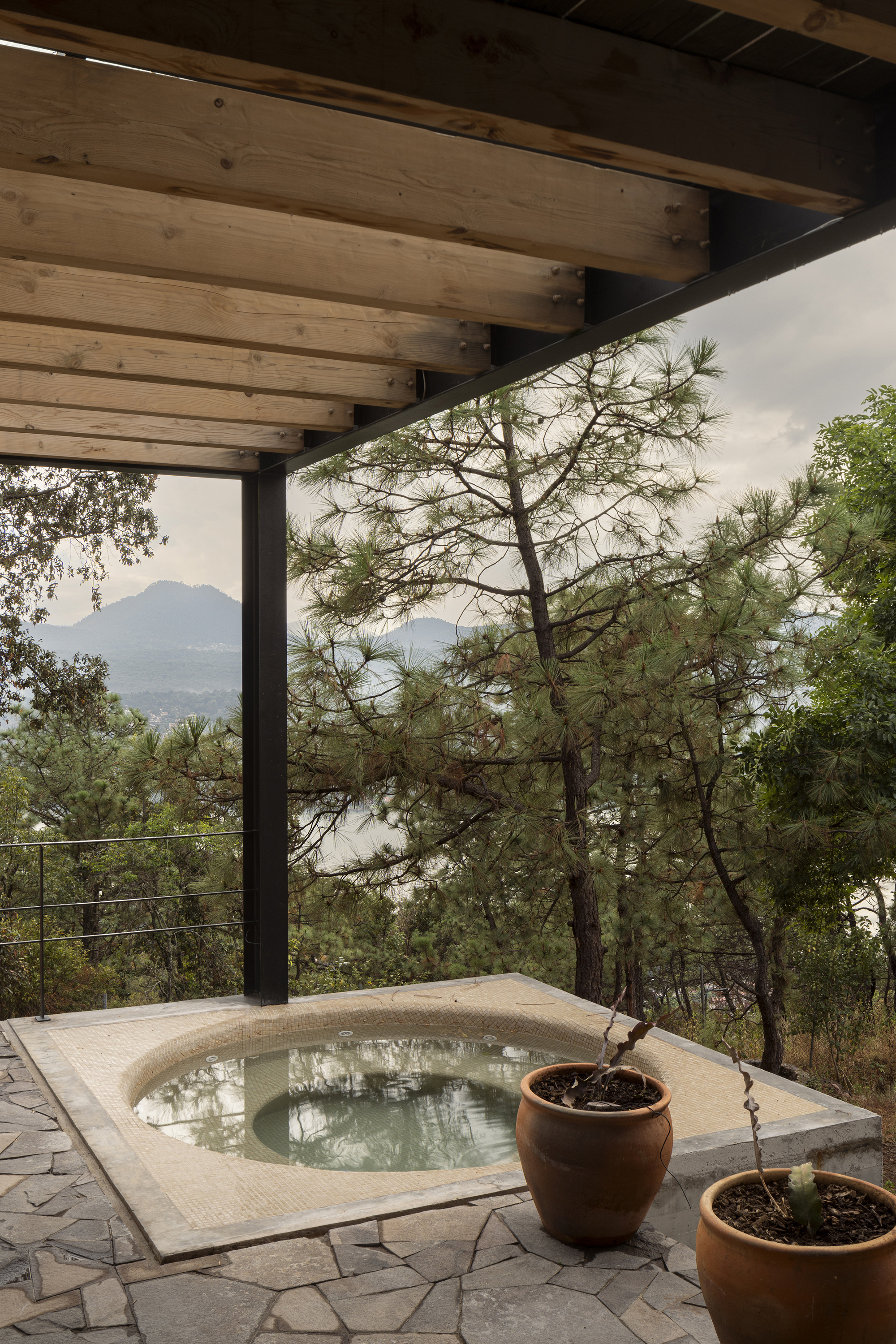Sunken stone-clad plunge pool on a terrace framed by timber beams and cable railing overlooking forested hills