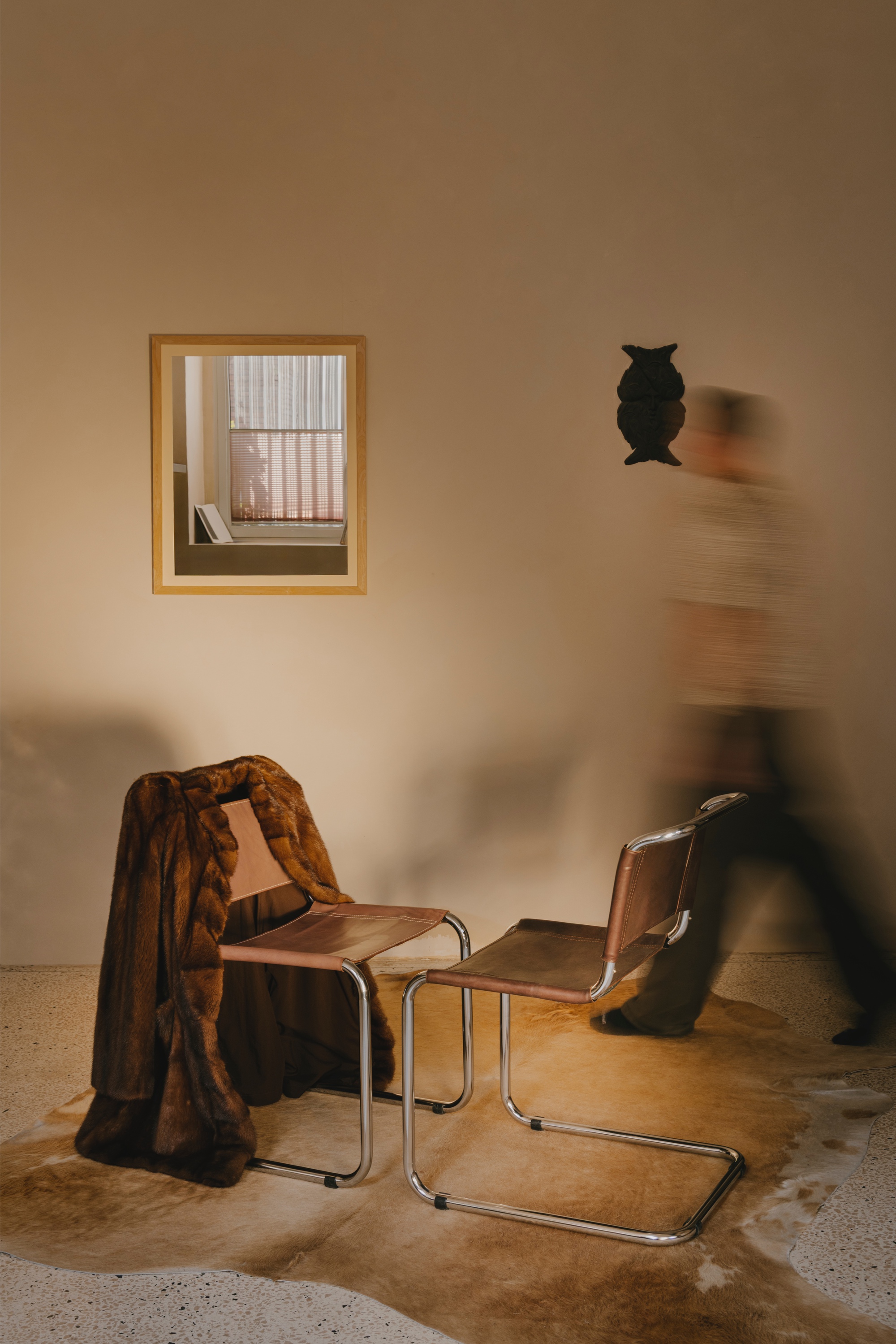 Timber-framed window niche and wall-mounted owl sculpture with figures moving past leather cantilever chairs