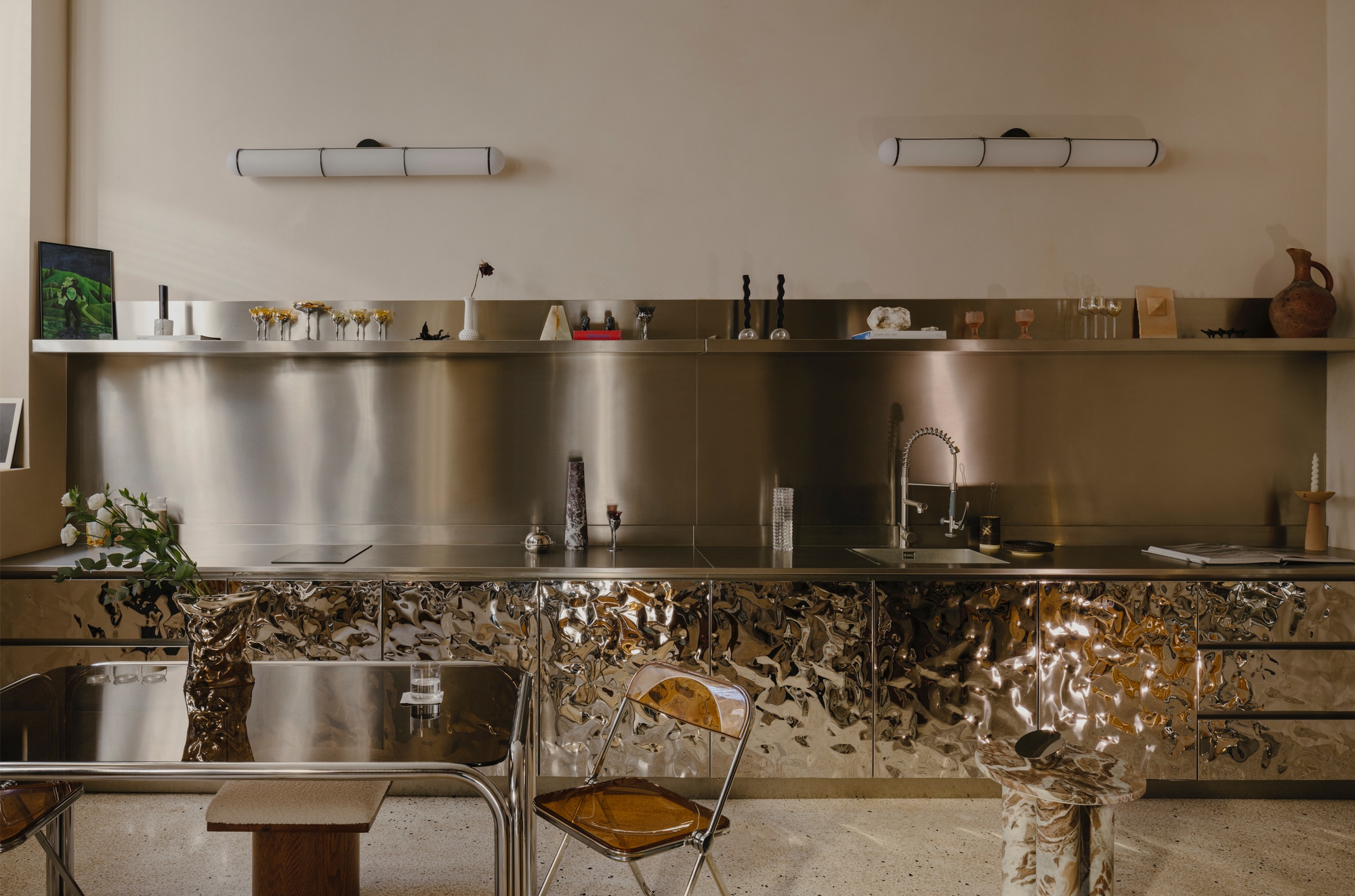 Kitchen with stainless steel backsplash and textured metallic cabinet fronts beneath a floating shelf