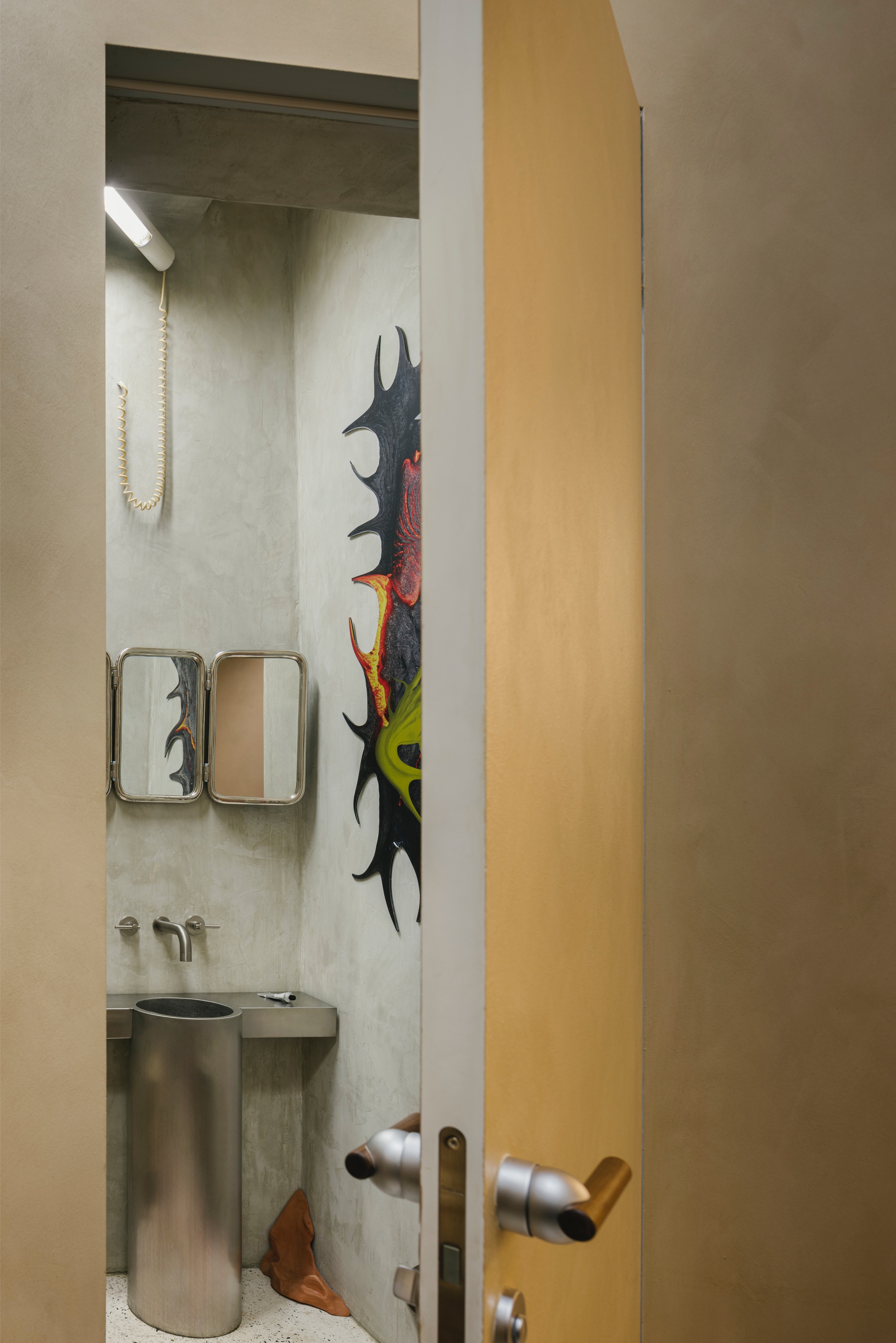 View through open timber door into bathroom with concrete sink and painted sculpture on wall