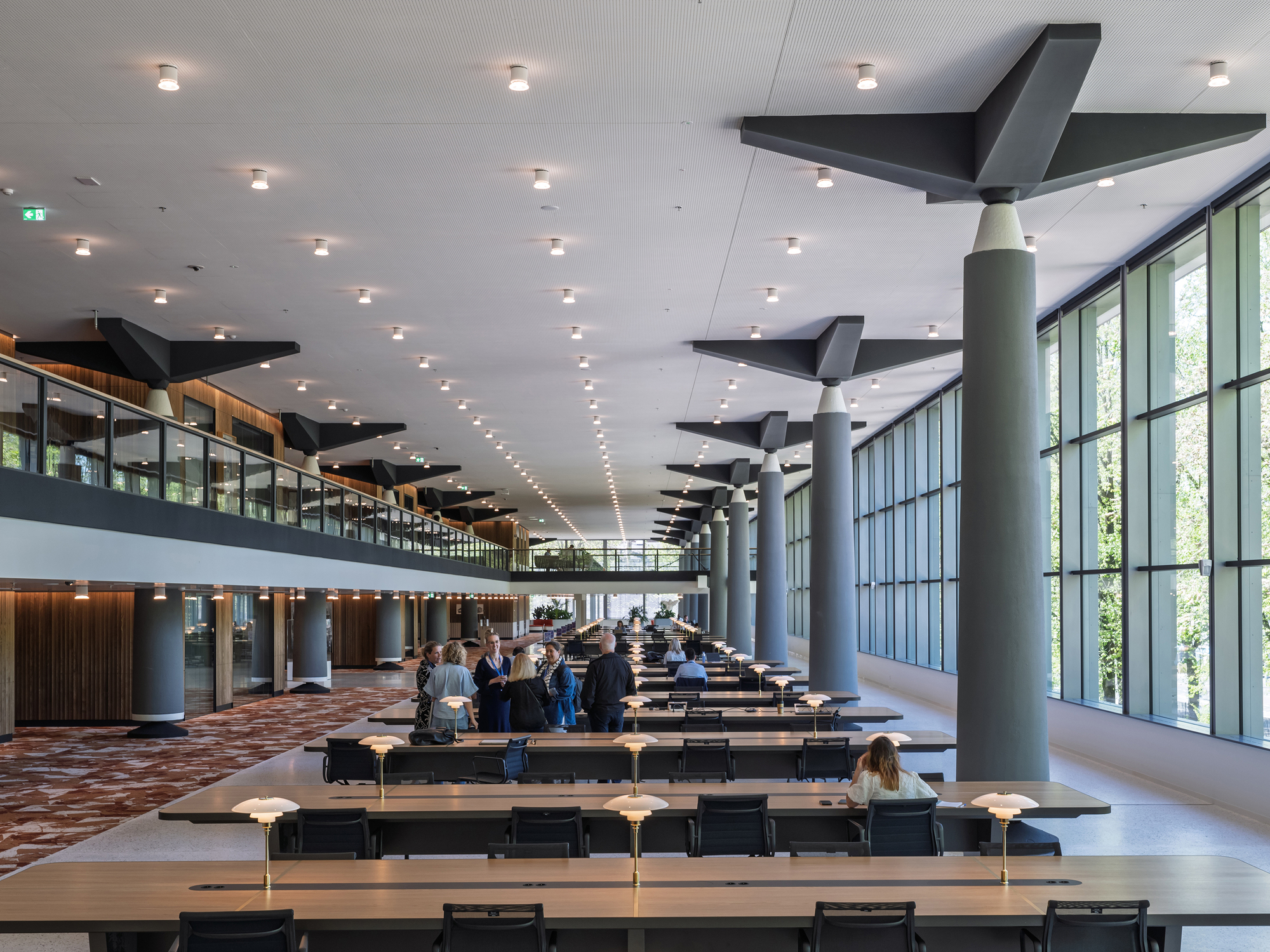 Double-height reading room with long study tables, cylindrical columns, and angular black ceiling baffles