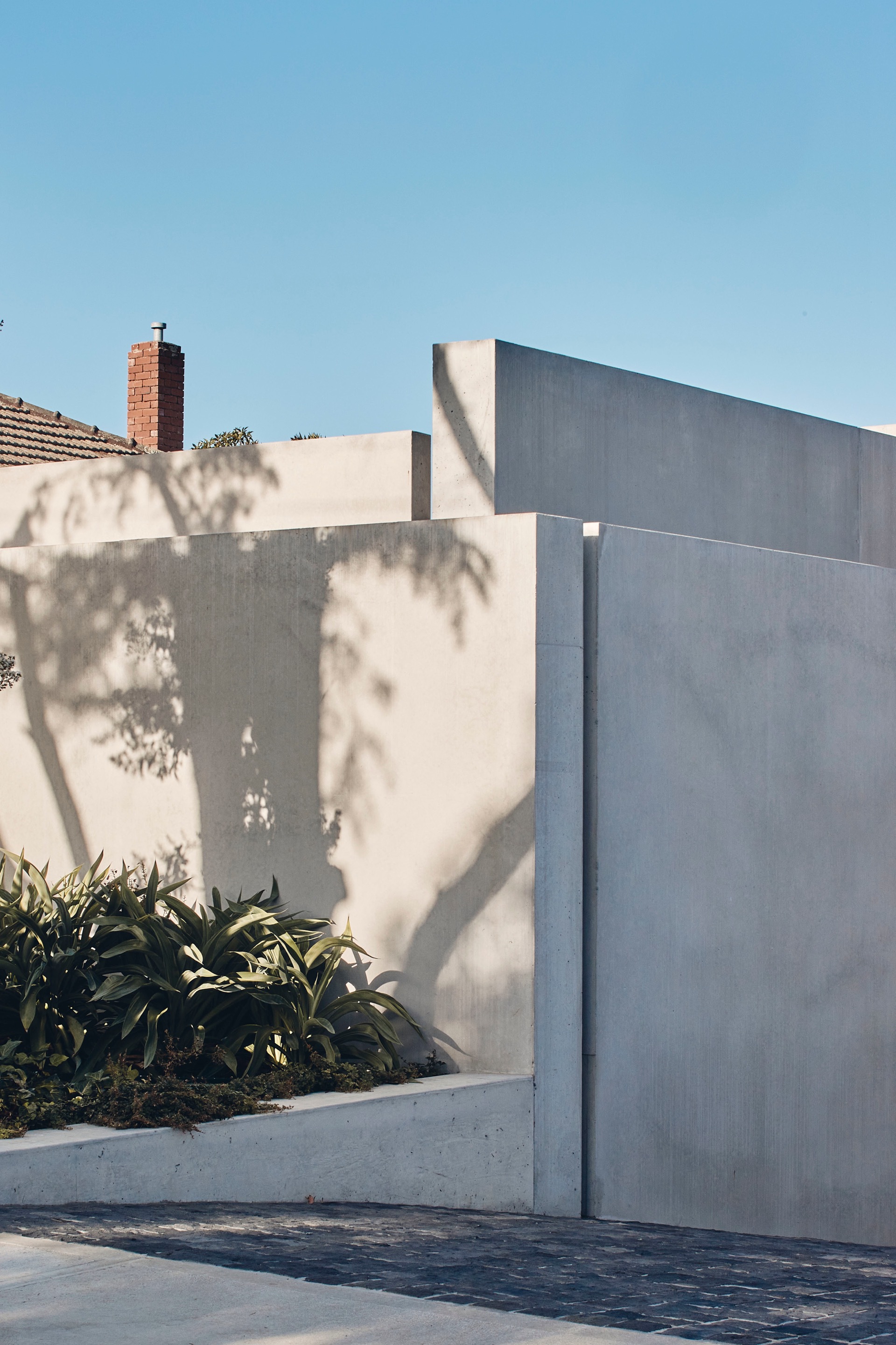 Corner detail of the concrete walls with tree shadows cast across the facade in morning light