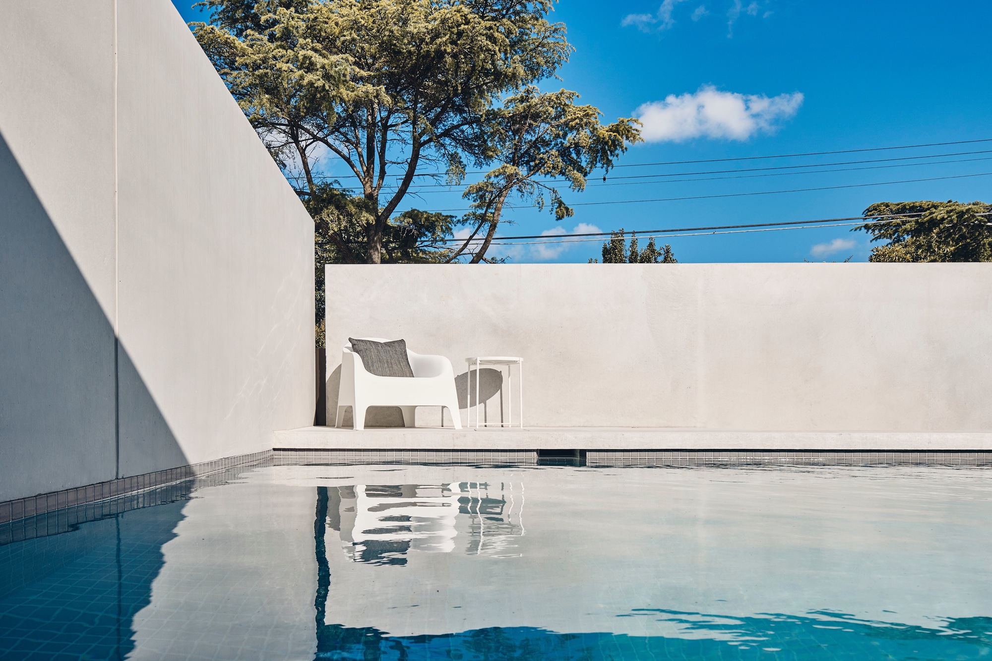 Pool terrace with white chairs reflected in still water under a clear blue sky