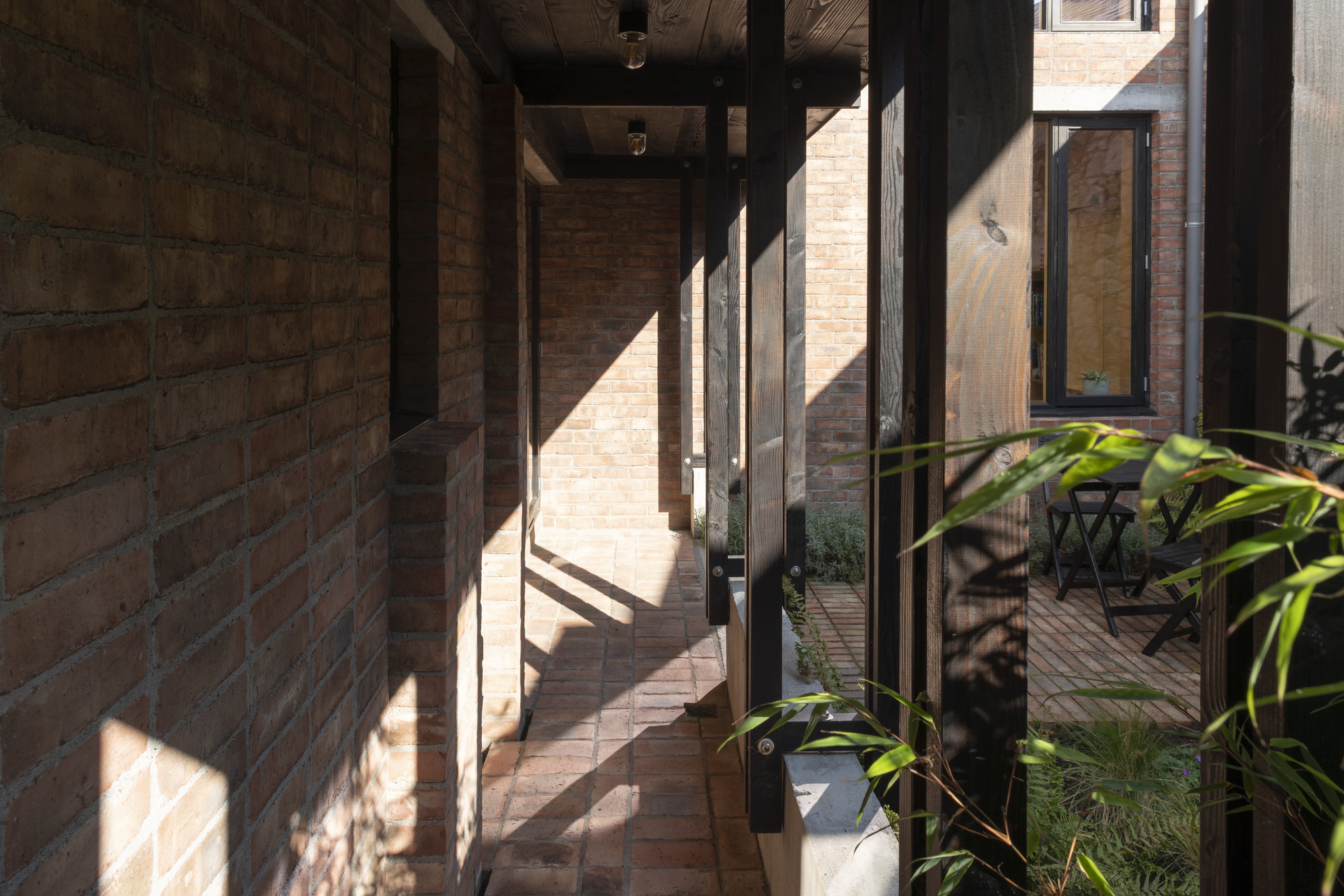 Glazed corridor with steel frame casting sharp shadows on brick walls and paved floor