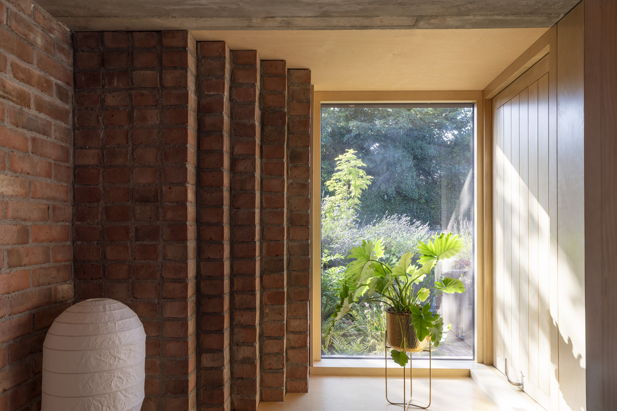 Corner niche with exposed timber joists and brick wall adjacent to picture window overlooking garden