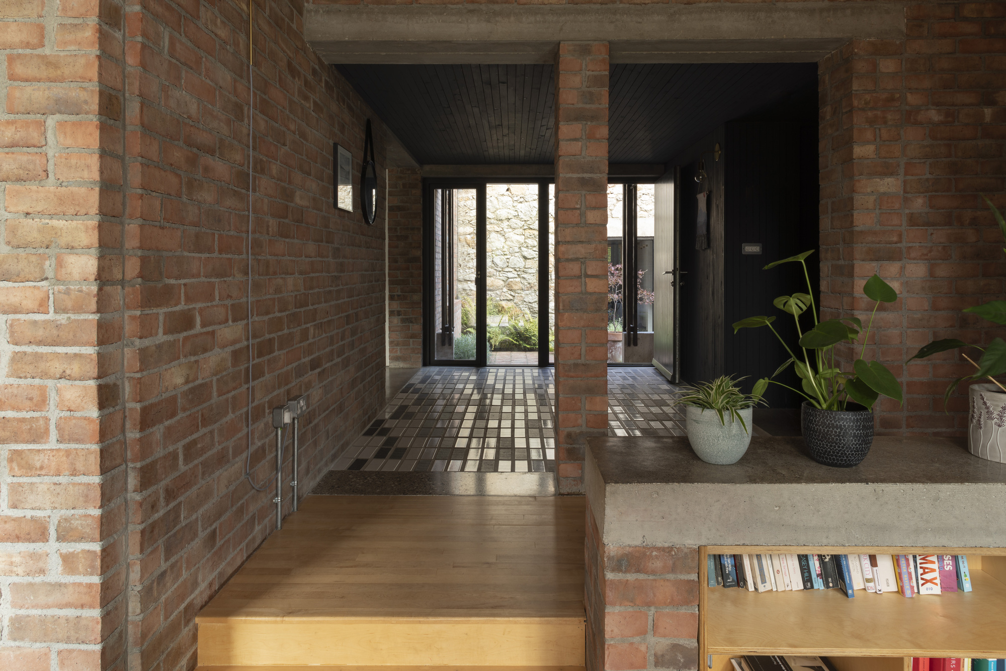 Entry corridor with brick walls and dark timber ceiling leading to glazed door and stone wall