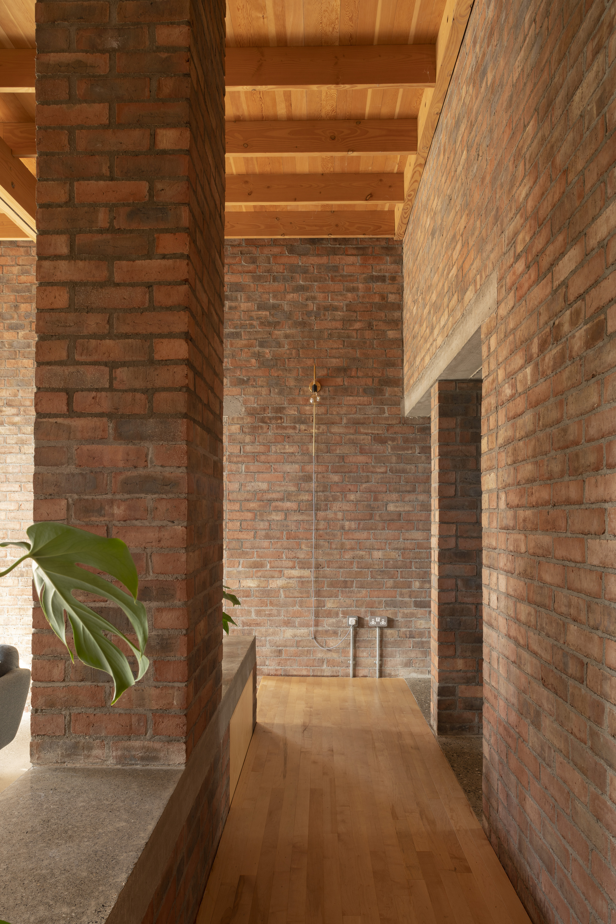 Interior passage framed by brick piers with a suspended pendant light and timber flooring in afternoon light