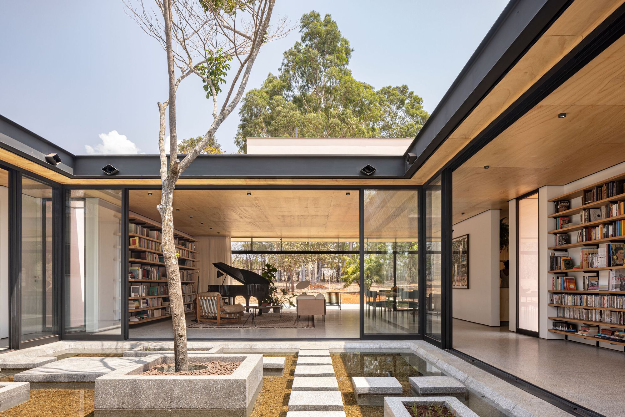 Internal courtyard with concrete planter bed, stepping stones over water, and glazed pavilions with timber ceilings