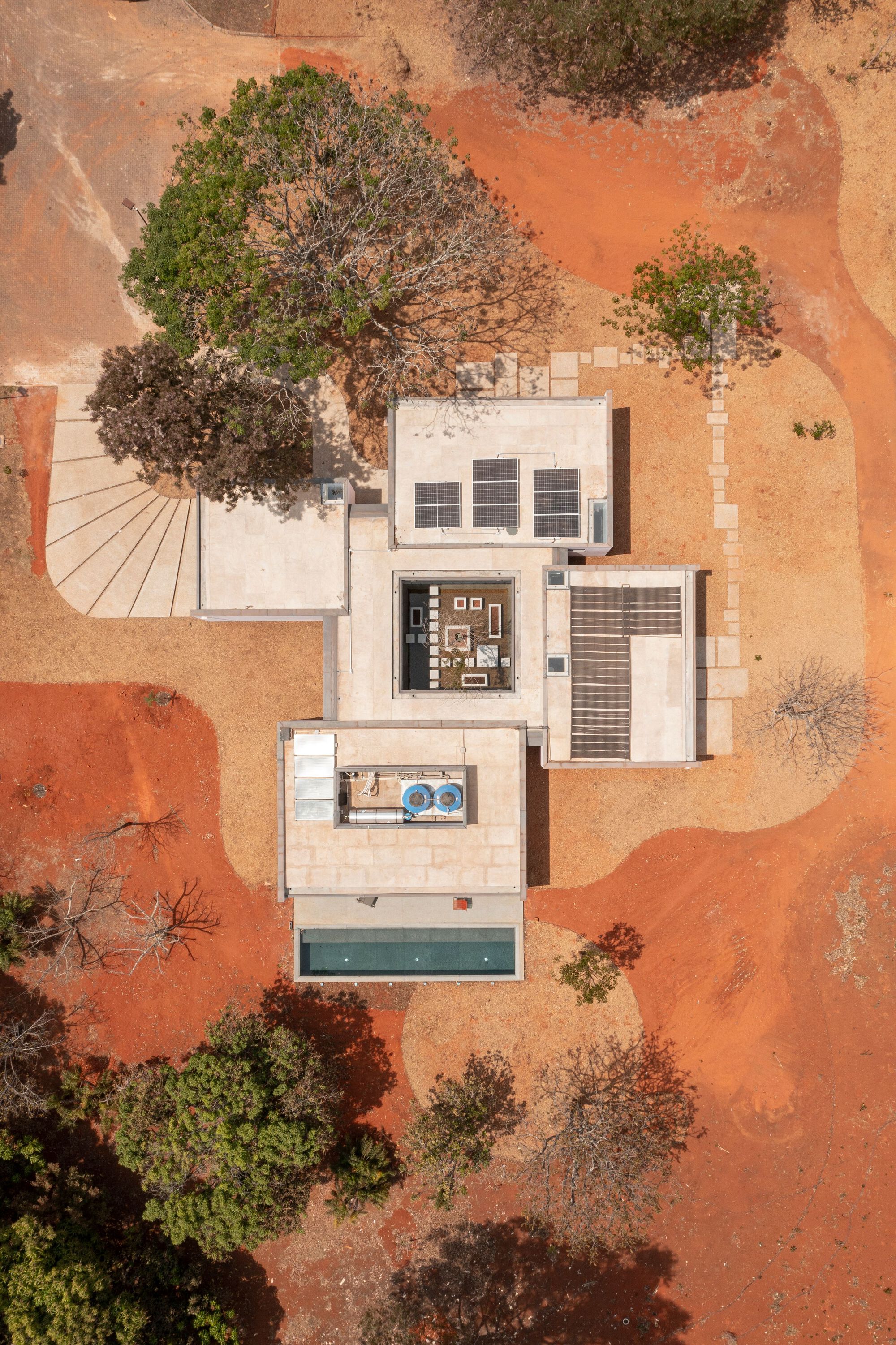Aerial drone view of white flat-roofed volumes with pool and courtyard on red earth terrain