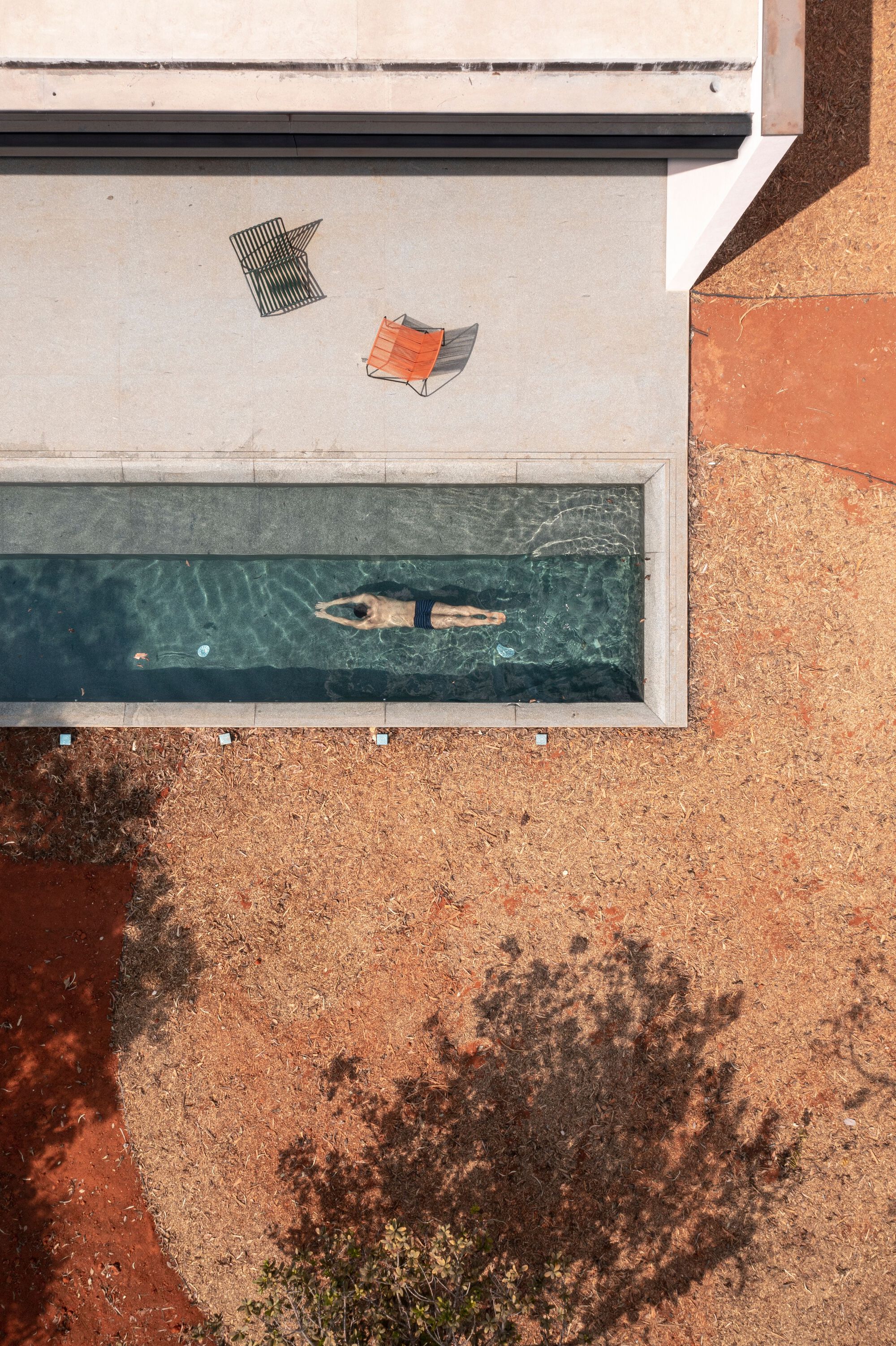 Aerial view of lap pool with swimmer beside orange gravel and two lounge chairs on deck