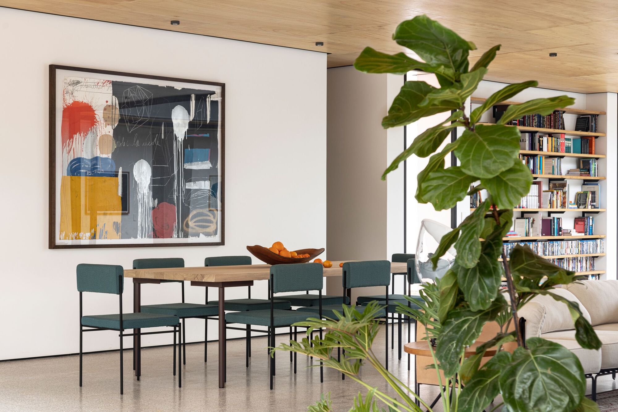 Dining area with round timber table and built-in bookshelves framed by a fiddle-leaf fig tree