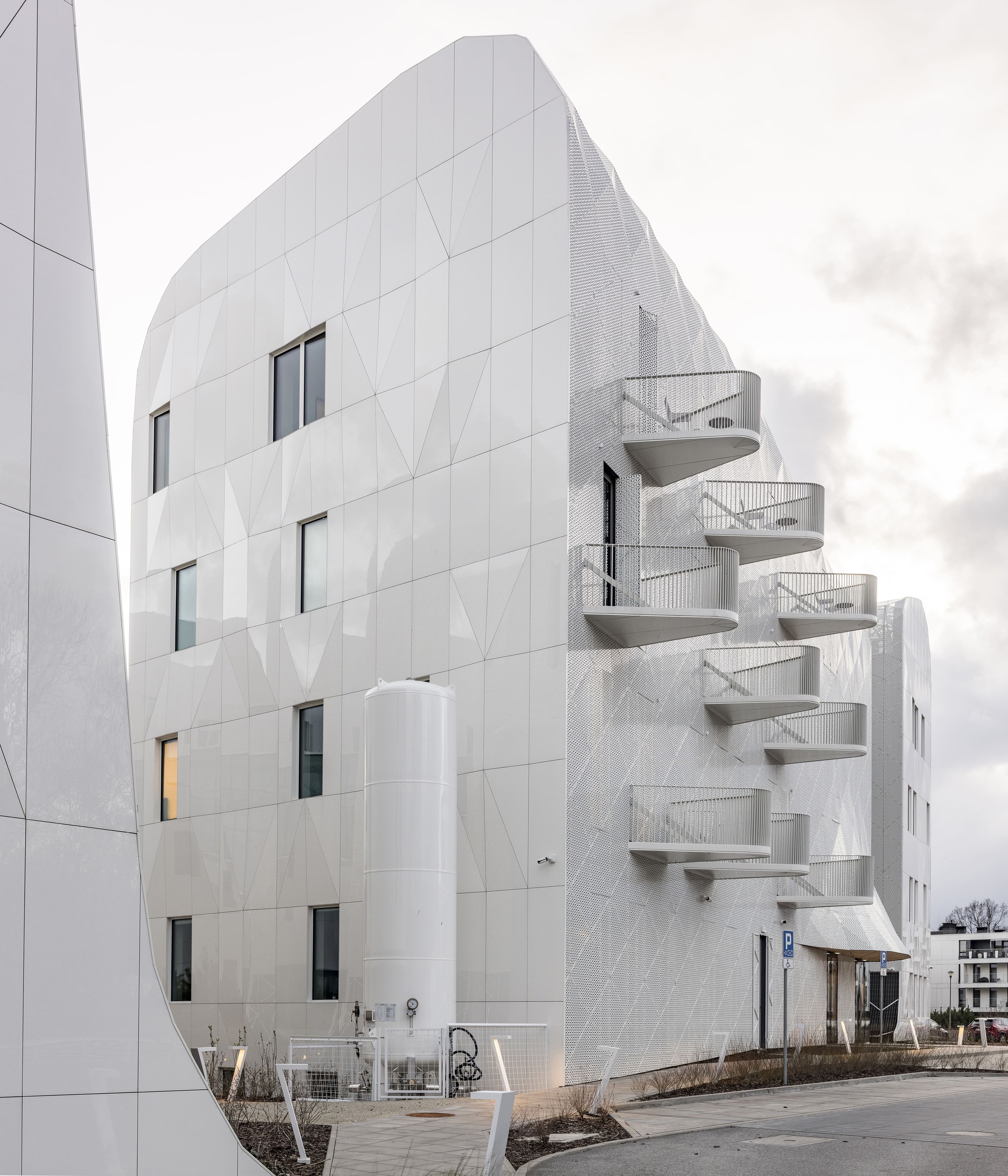 White paneled facade with stacked triangular balconies and punched windows under an overcast sky