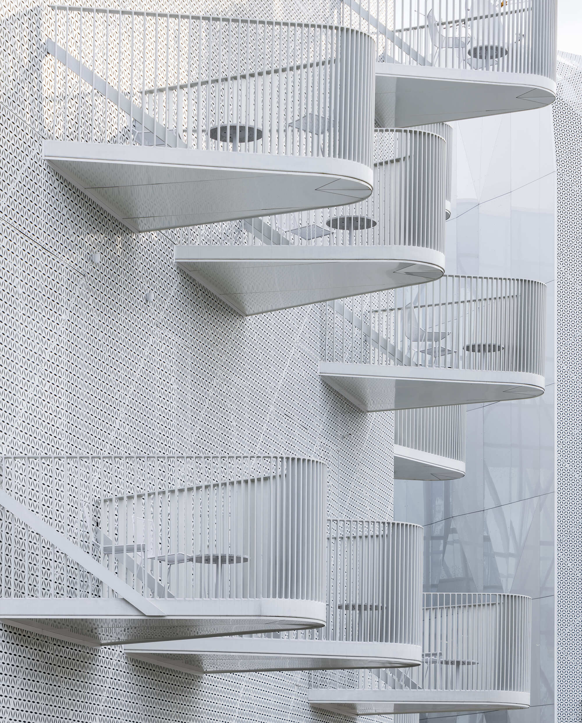 White spiral staircase with perforated metal walls and curved treads in diffuse light