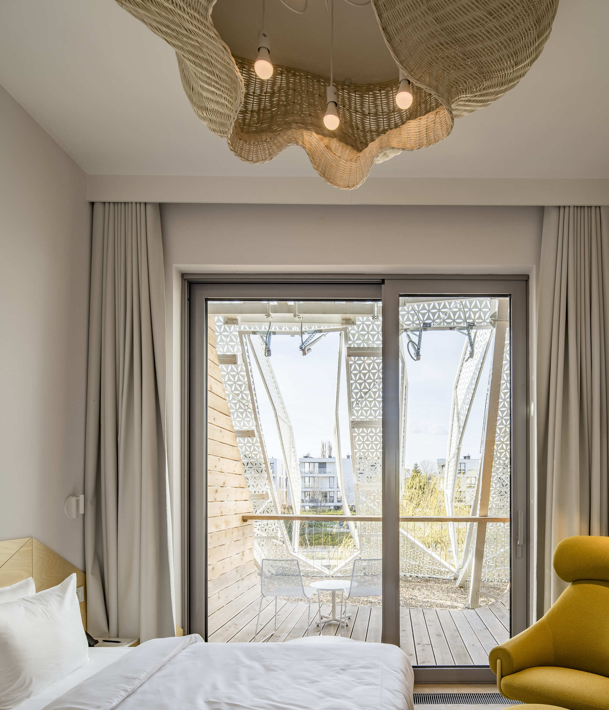 Bedroom with sliding glass doors opening to a timber deck with woven basket pendant above