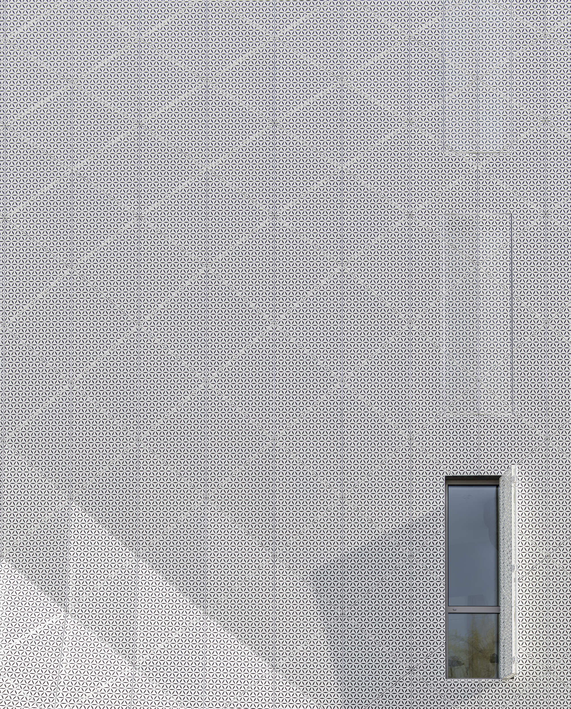 White perforated metal facade with a single narrow vertical window opening
