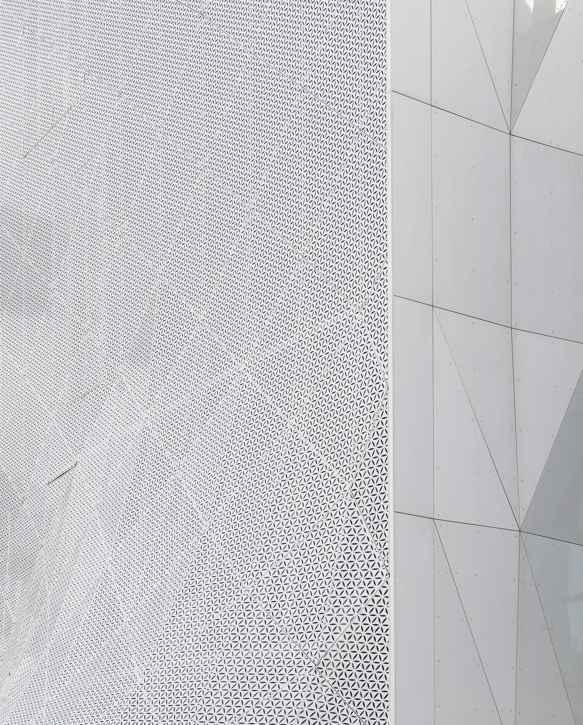 Corner detail where perforated white metal cladding meets smooth flat paneling