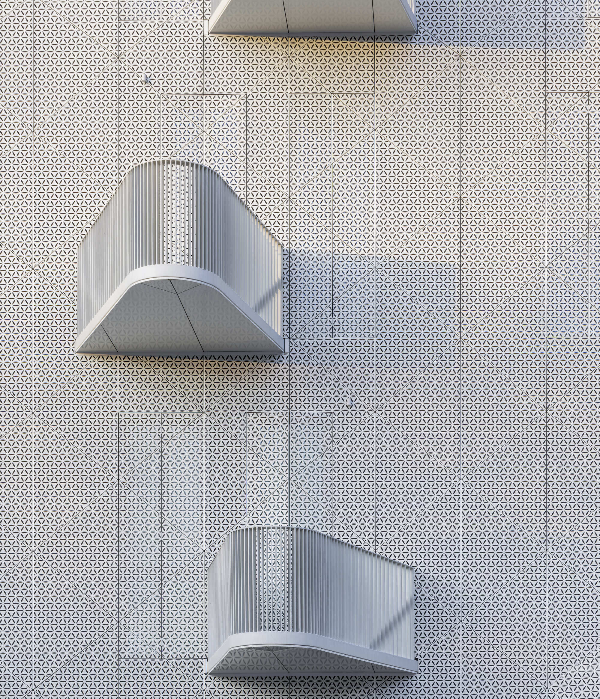 Overhead view of curved metal canopies projecting from a perforated white facade