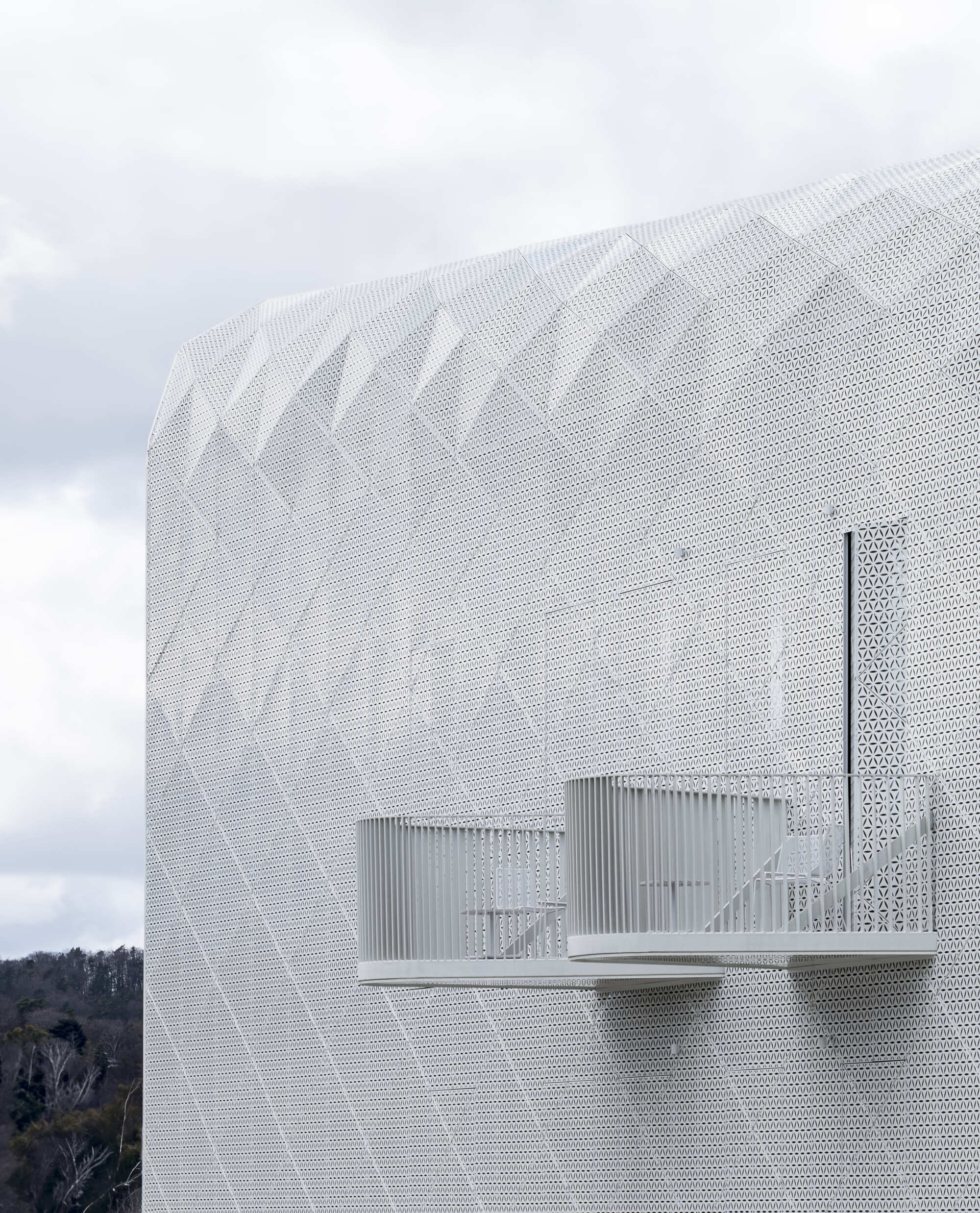 Side view of a curved perforated metal volume with canopy openings under cloudy skies