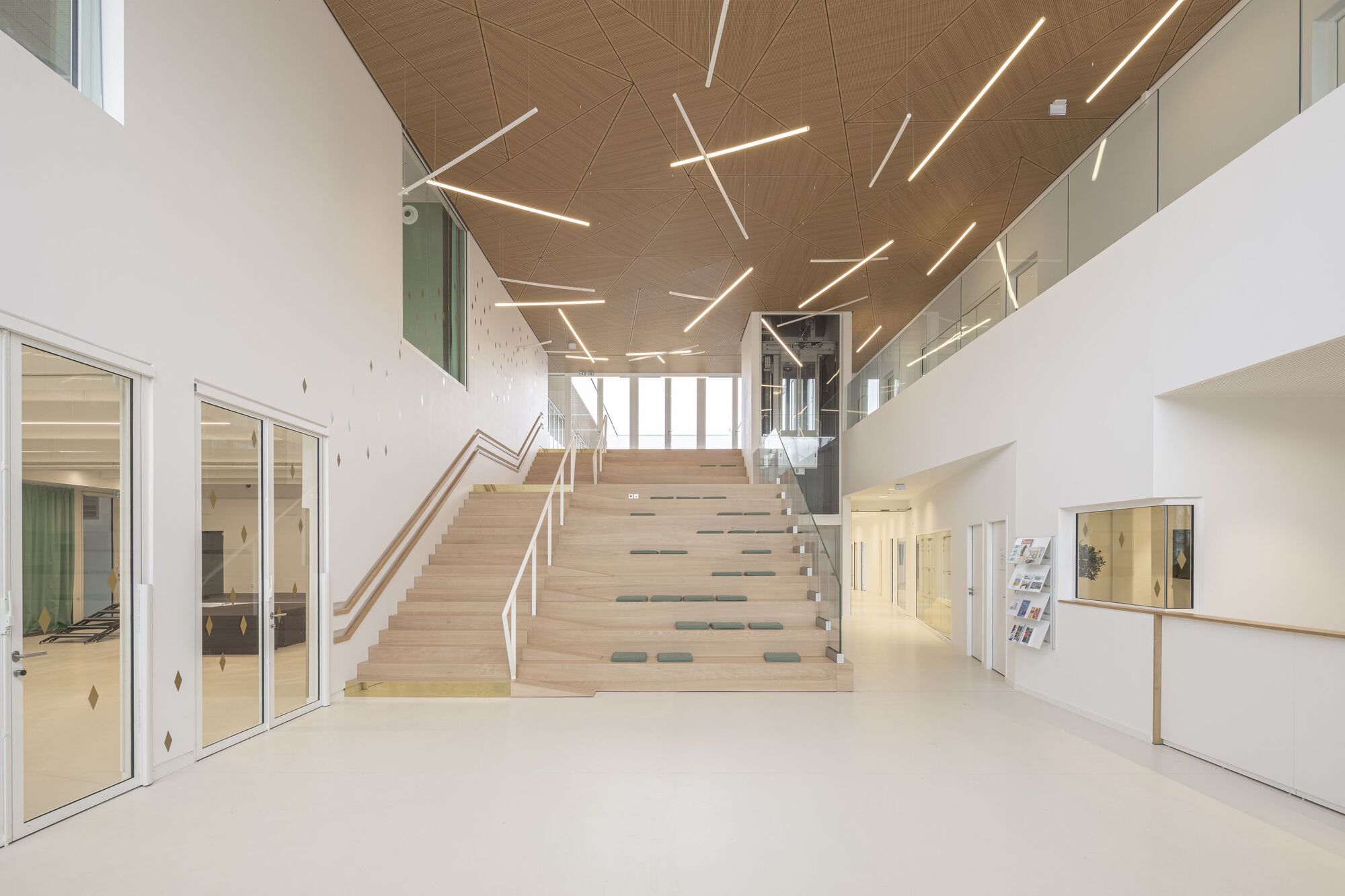 Central timber staircase ascending beneath a wooden ceiling with geometric linear lighting fixtures in the entrance hall