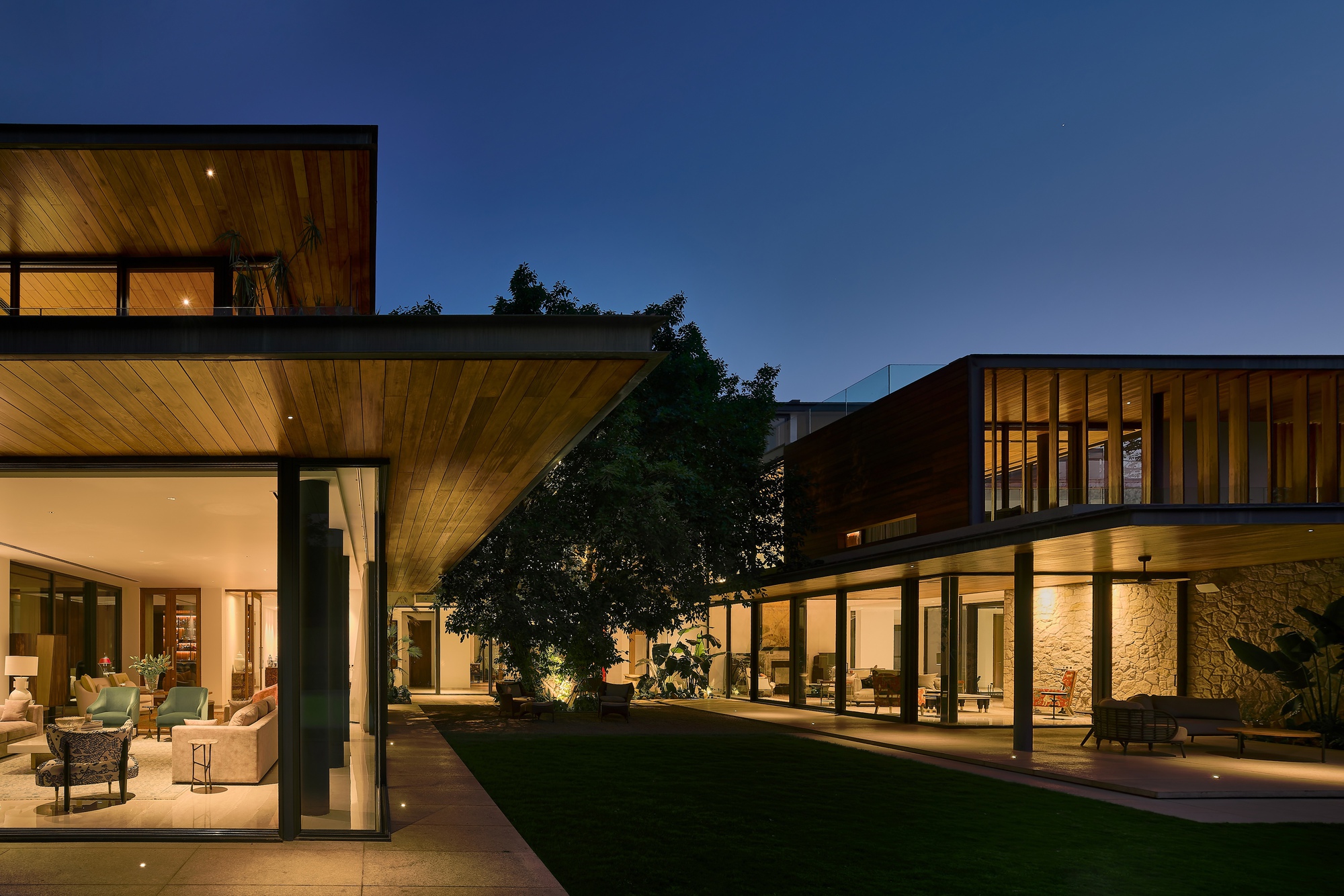 Courtyard view at twilight showing two wings with timber ceilings and lit stone wall between