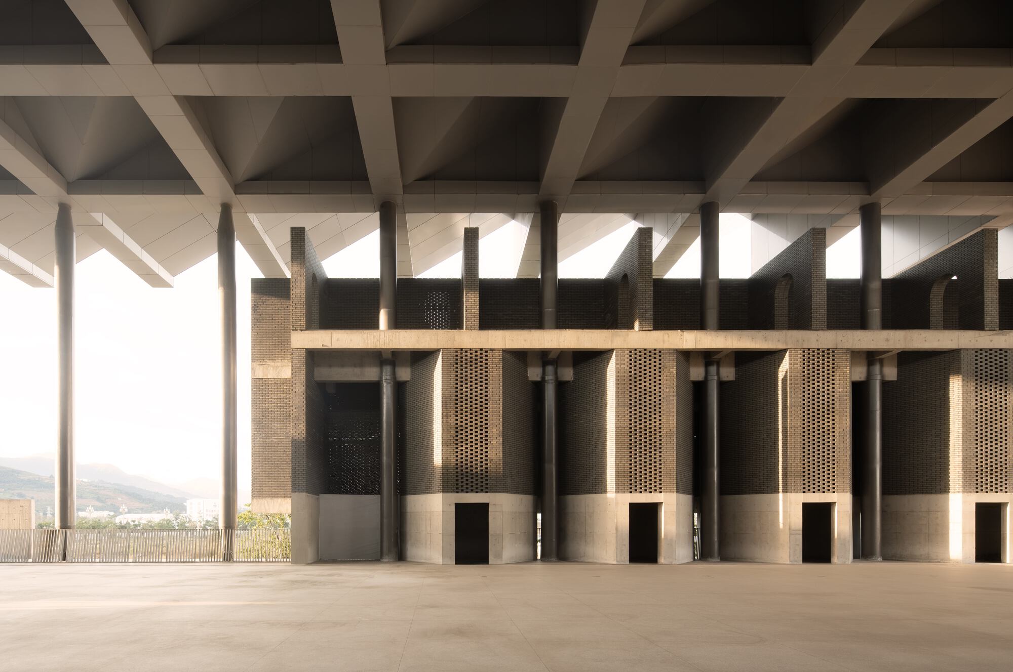 Interior row of perforated bronze cylindrical columns beneath a coffered concrete ceiling