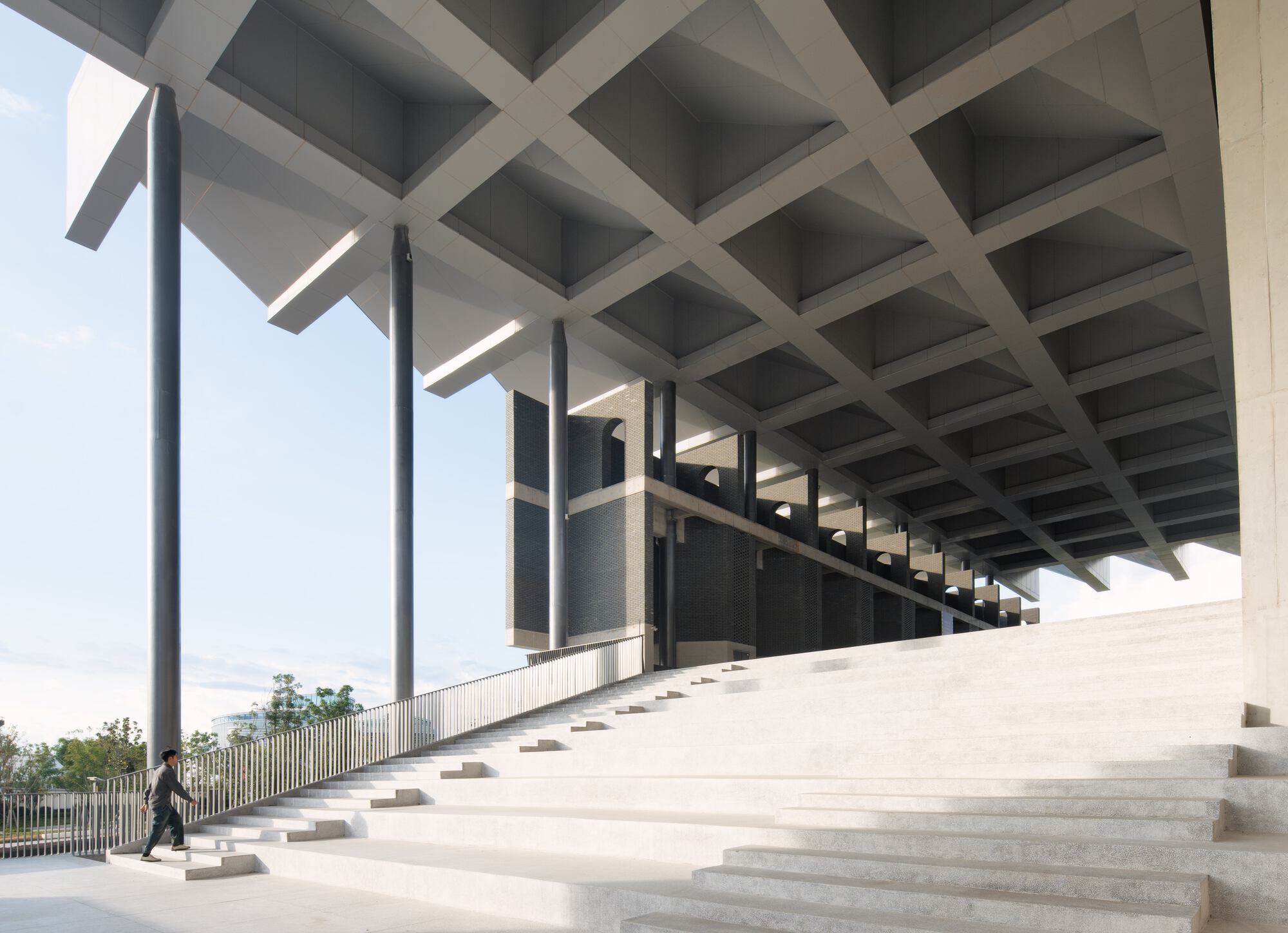Wide ceremonial staircase beneath a coffered concrete ceiling with a lone figure walking at the base