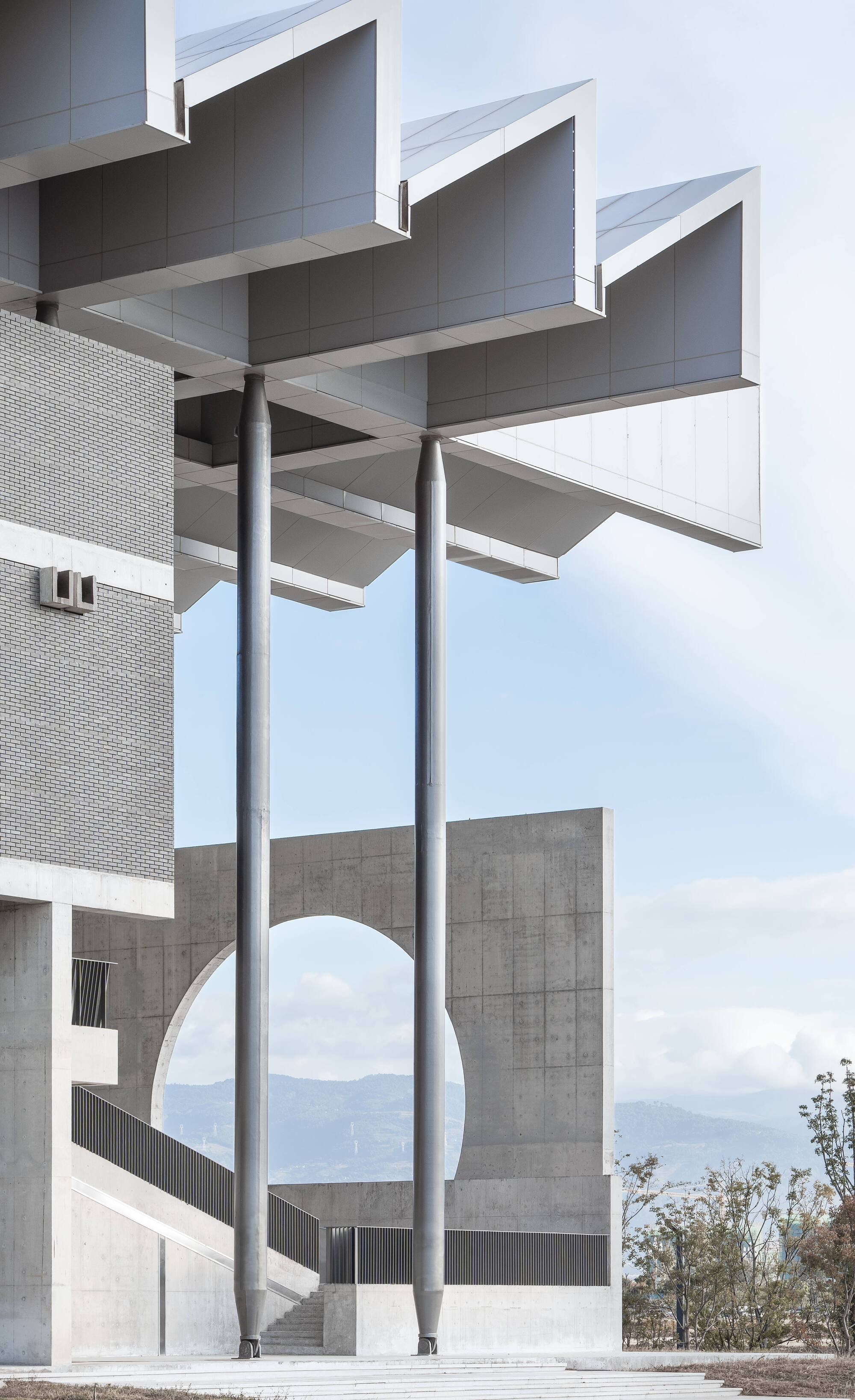 Steel columns supporting stacked concrete beams and sawtooth canopy against a cloudy mountain backdrop