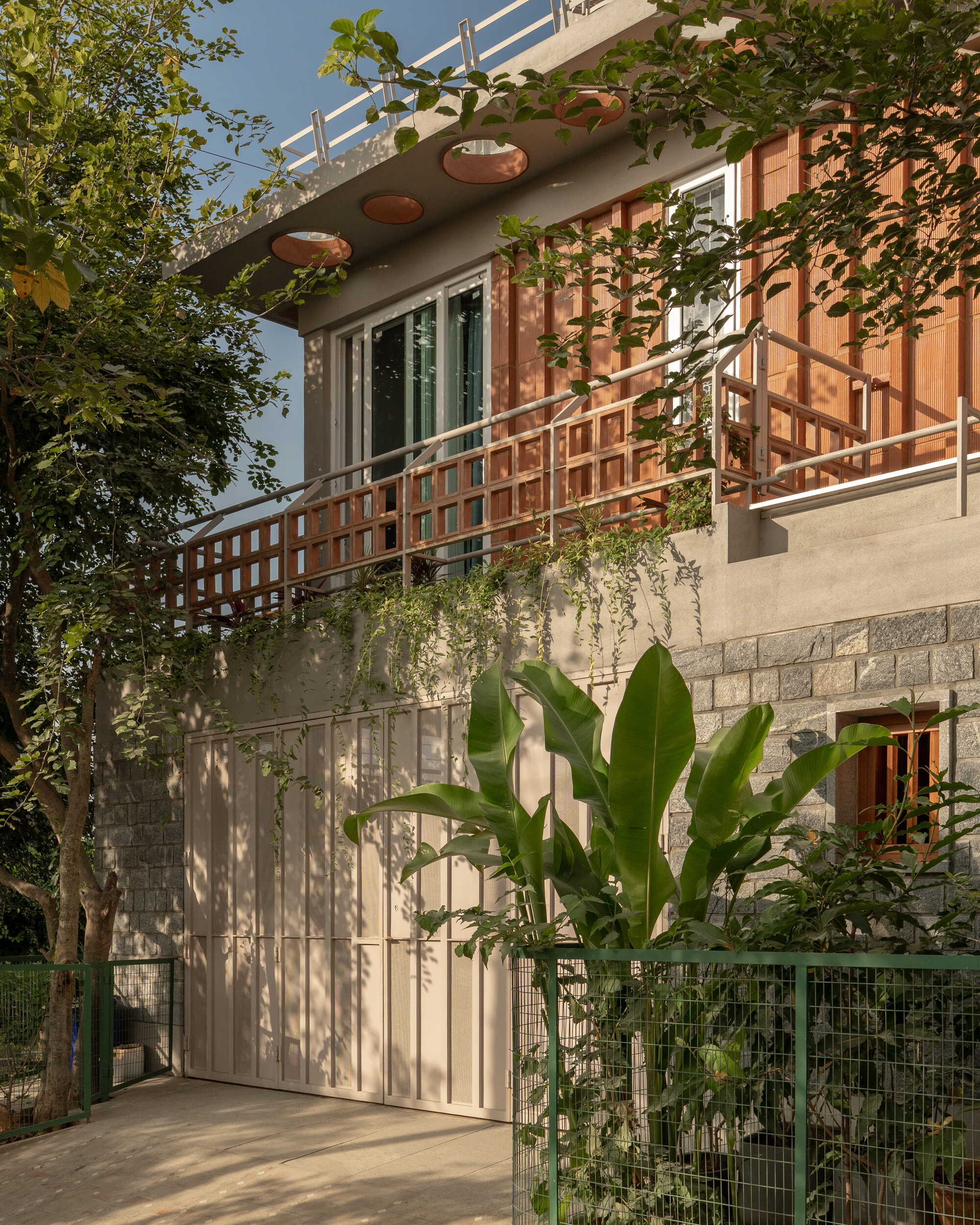 Detail of the timber grid railing and terracotta circular roof penetrations with banana plants in afternoon light