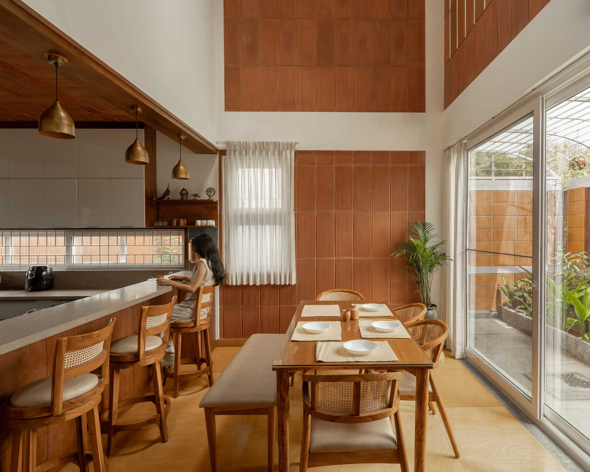 Dining area with terracotta tile wall panels and glazed doors opening to a planted courtyard in daylight