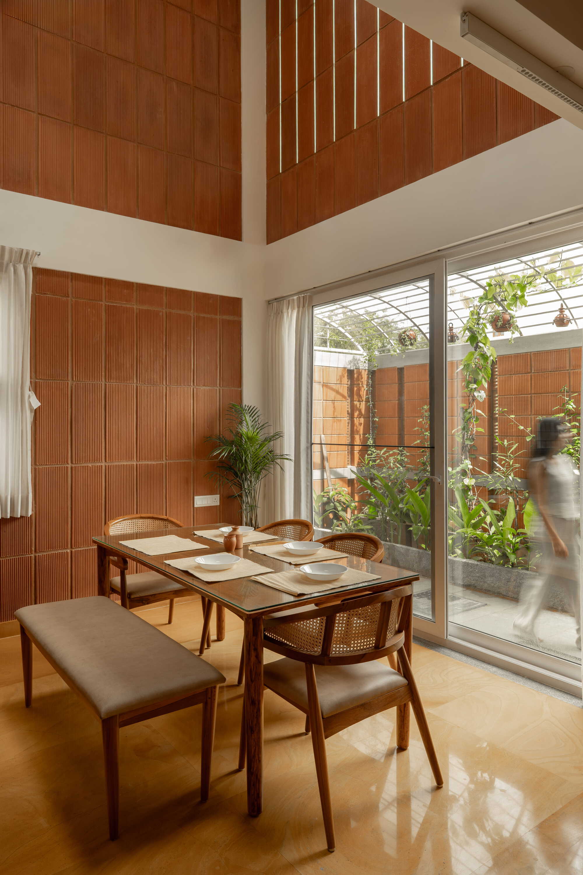 Dining table beside floor-to-ceiling glass doors with a person moving through the adjacent planted courtyard