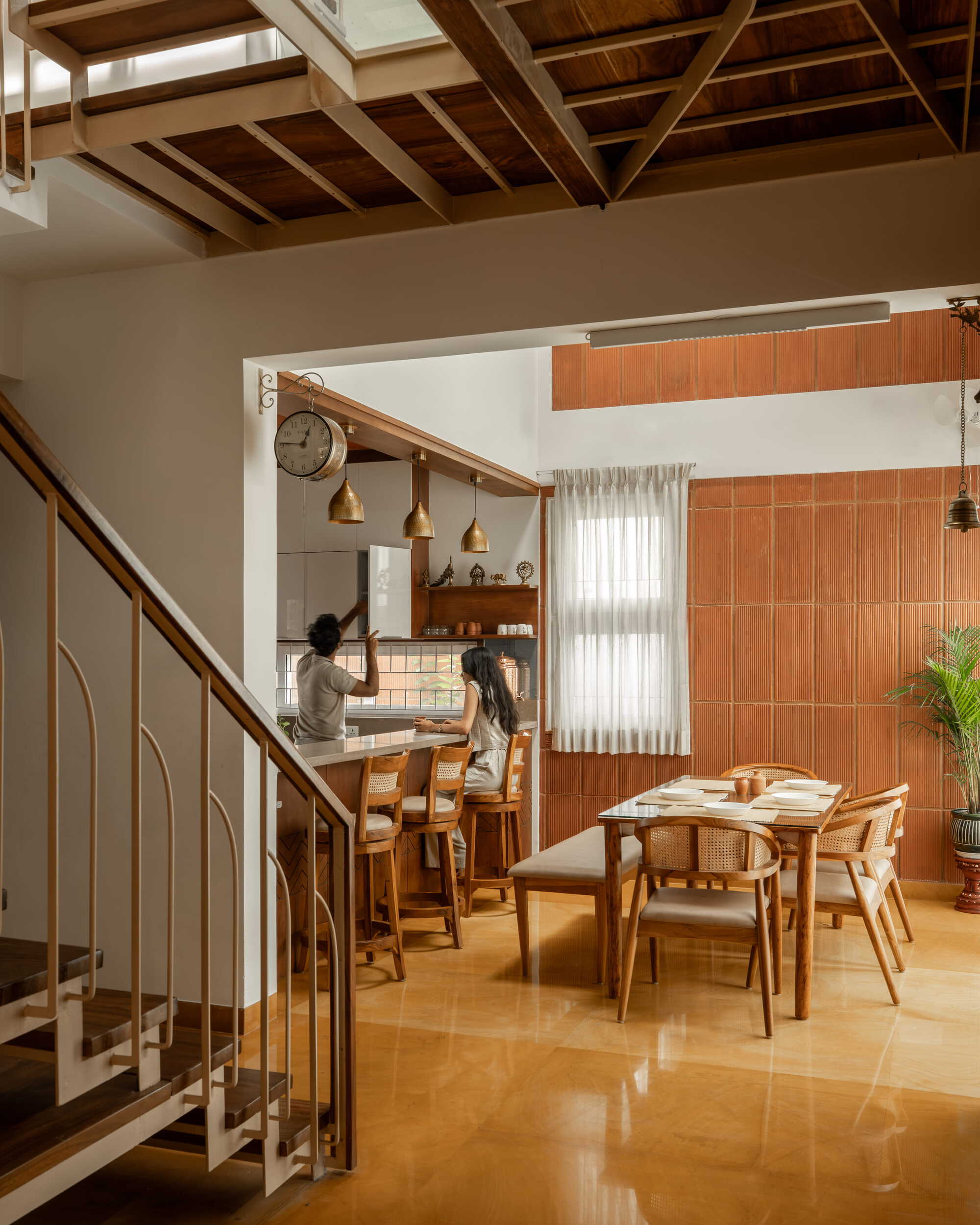 Double-height living and dining space with exposed timber ceiling beams and a steel balustrade staircase