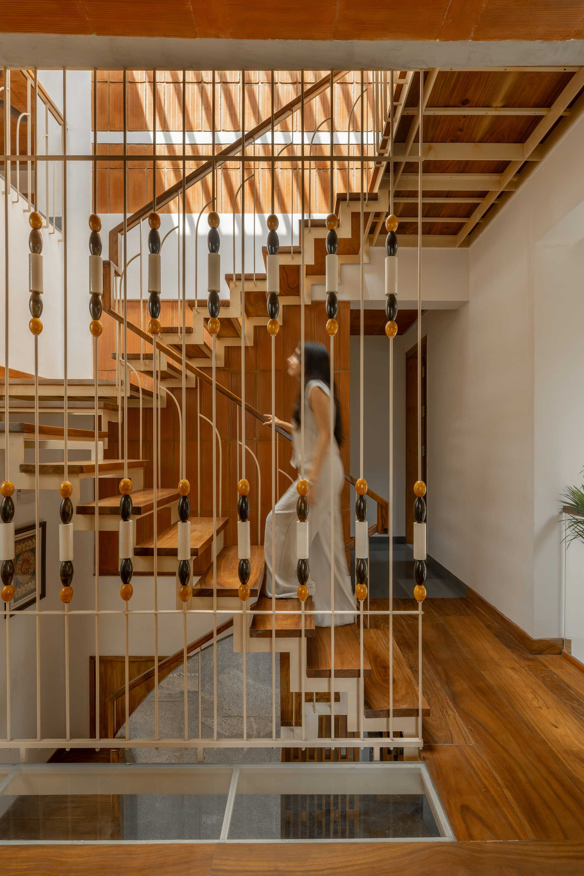 Open timber staircase with brass balustrade and carved wooden details rising through a double-height space