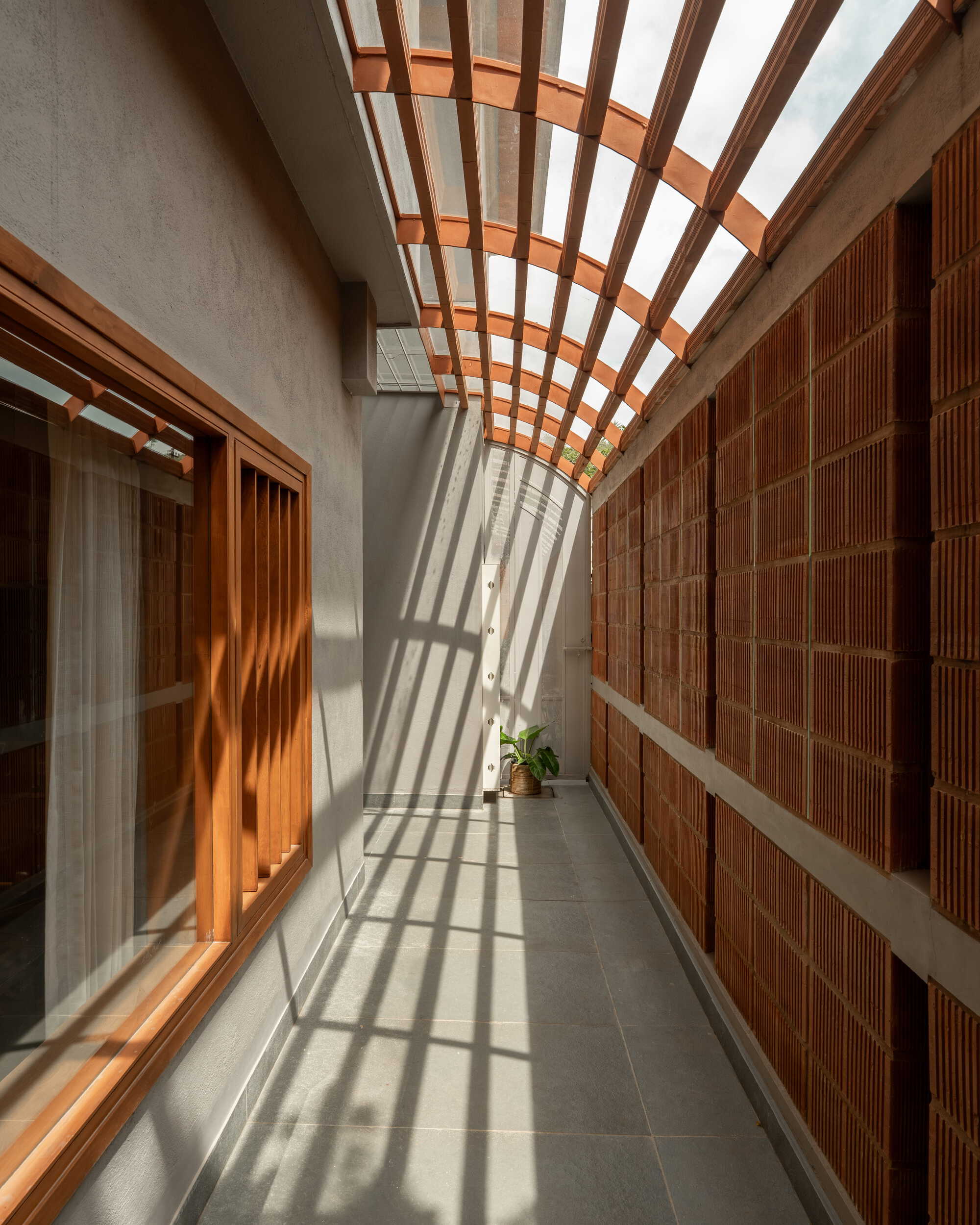 Narrow corridor with timber trellis overhead casting striped shadows across the concrete floor