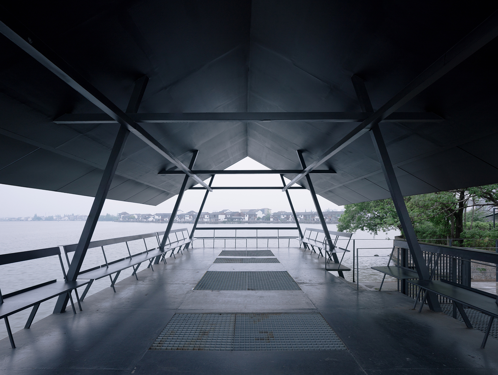 Covered platform with diagonal steel bracing and folded ceiling panels framing a view of the lake