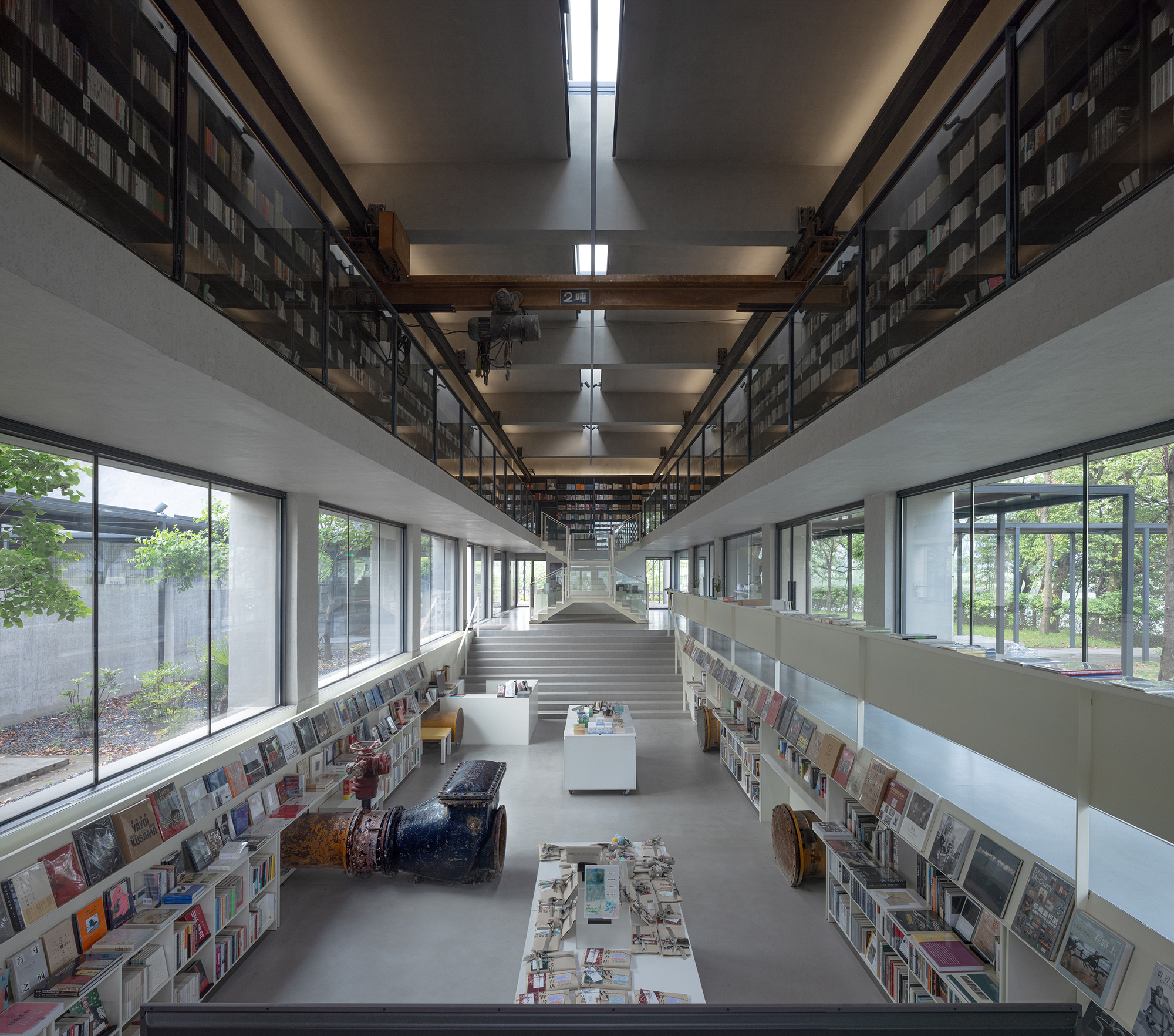 Double-height library interior with central staircase flanked by bookshelves and courtyard windows on both sides